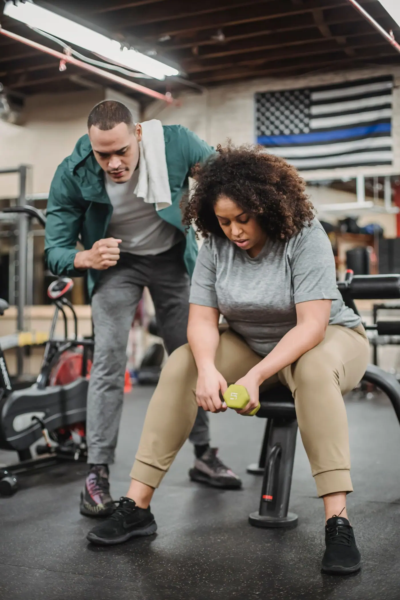A personal trainer helping an adult exercise safely with a dumbbell.