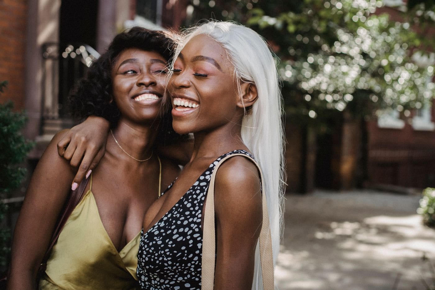 Two friends laughing and hugging outdoors.