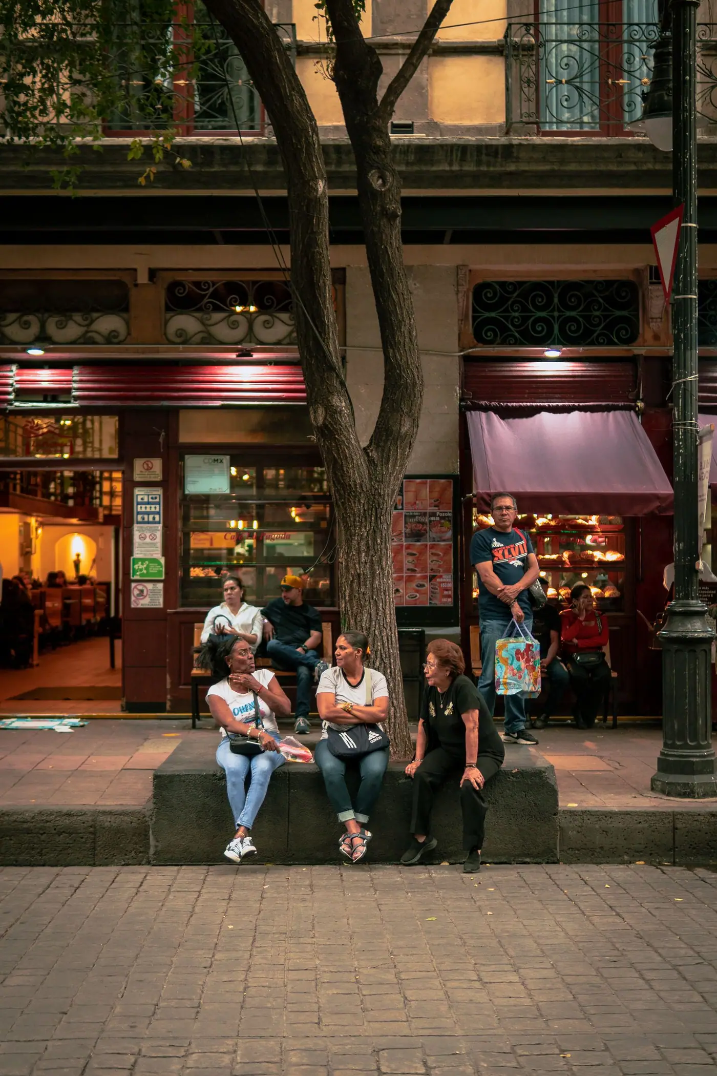 A group of people sitting and talking on a bench outside a café in Mexico City.