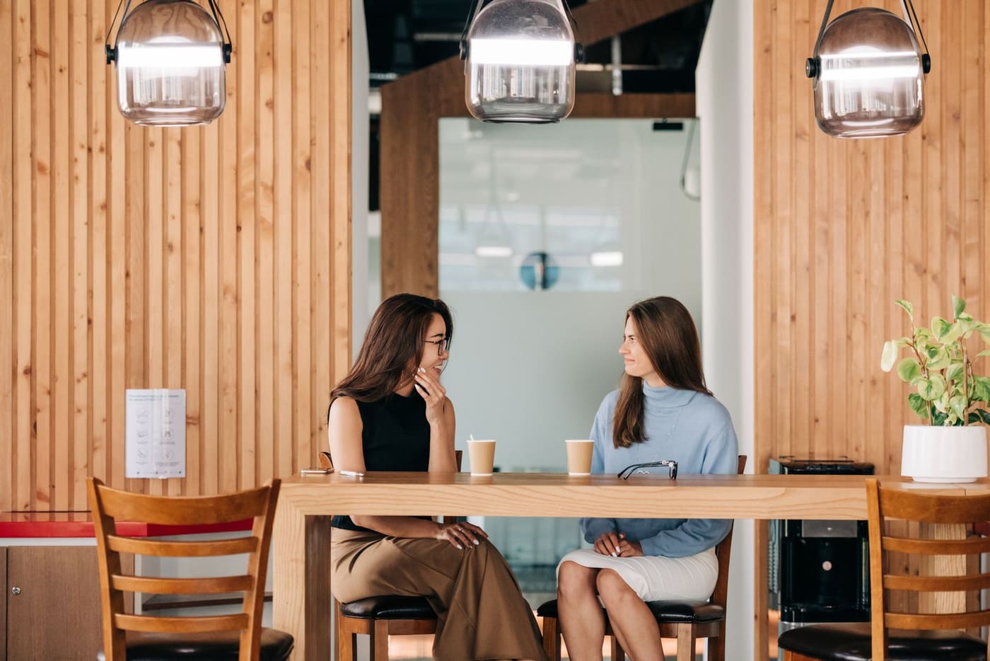 Two friends smiling and talking over coffee at a cafe table.