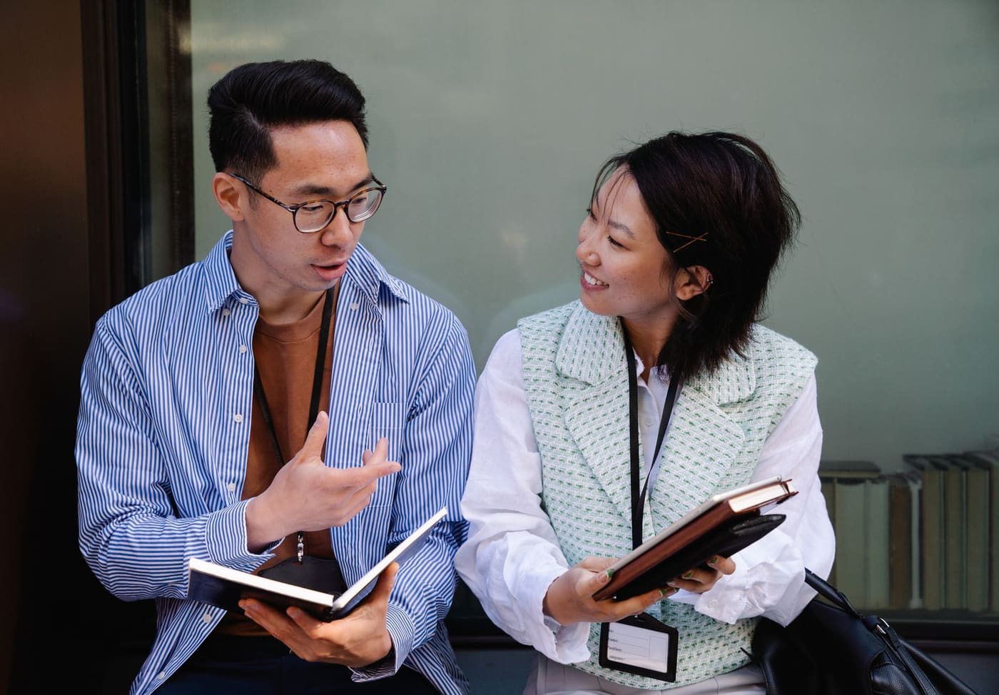 Two adults talking together while holding notebooks.