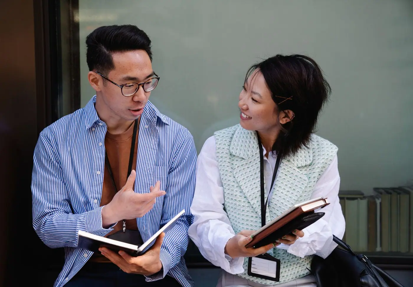 Two adults talking together while holding notebooks.