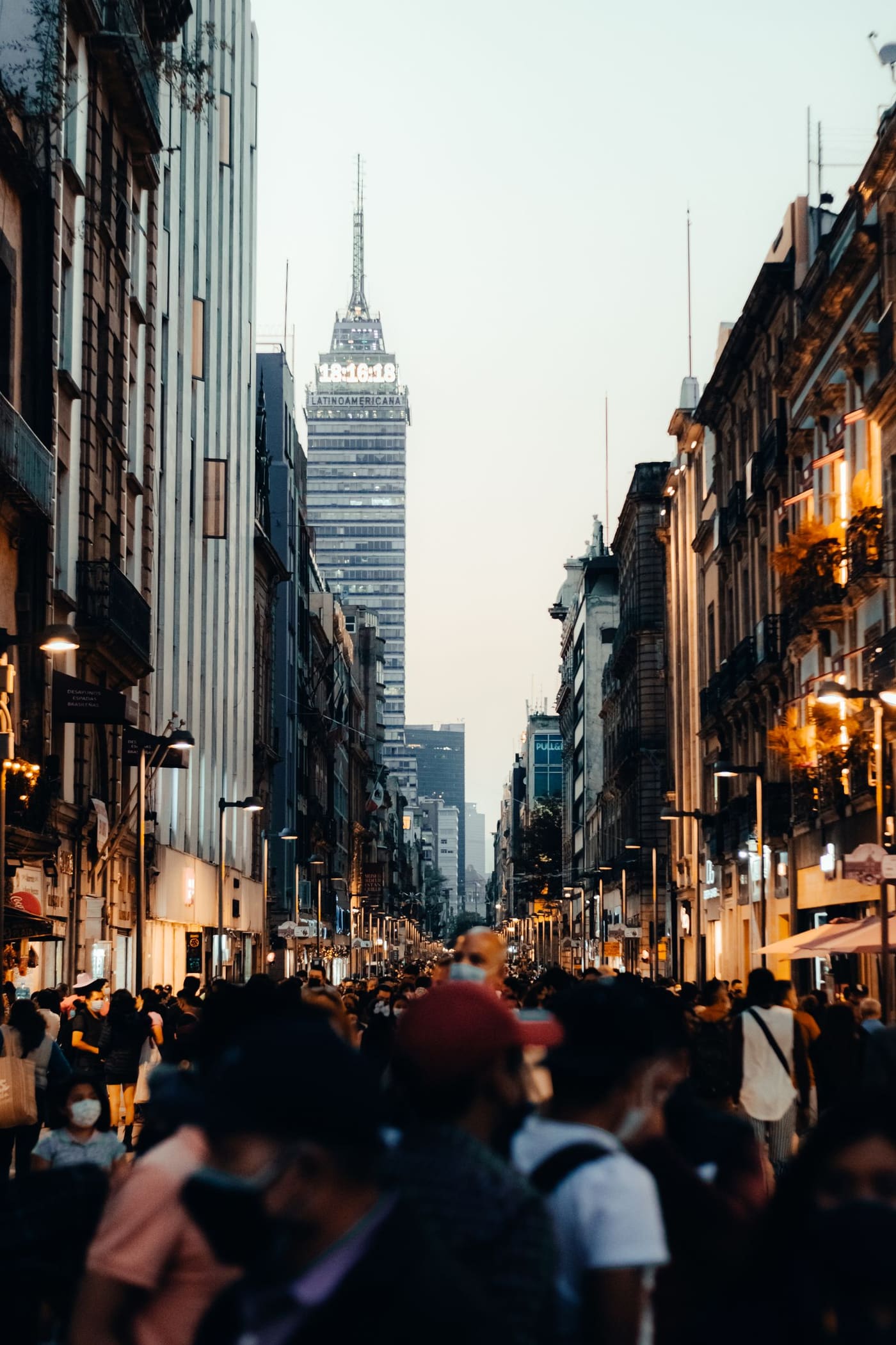 A crowded Mexico City street with Torre Latinoamericana at dusk.