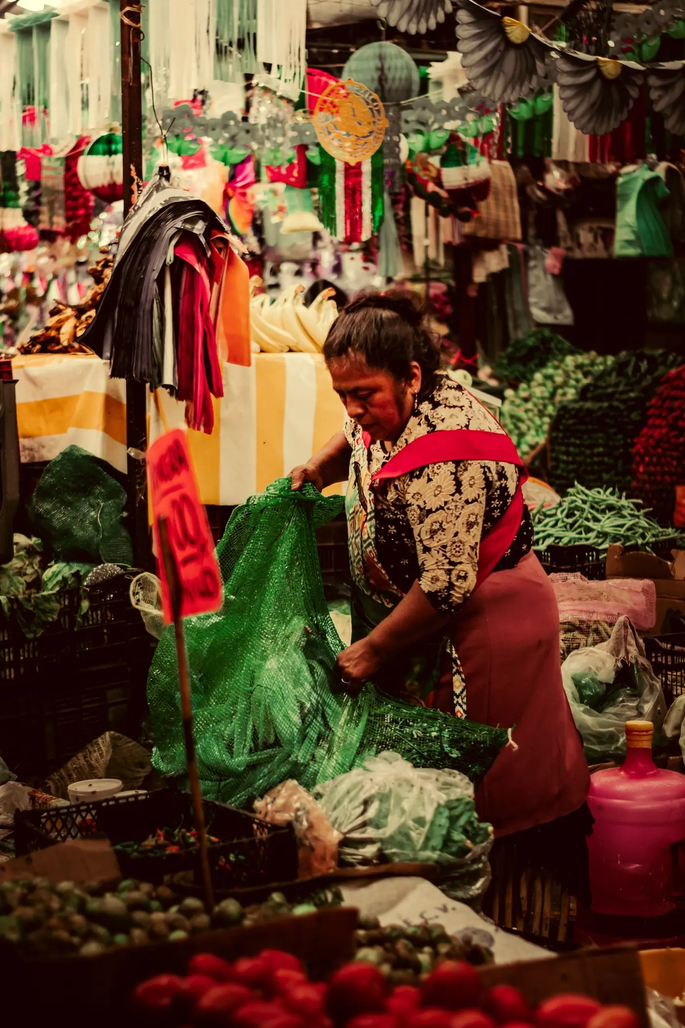 A woman lifting a green mesh sack of produce at a market stall in Cholula.