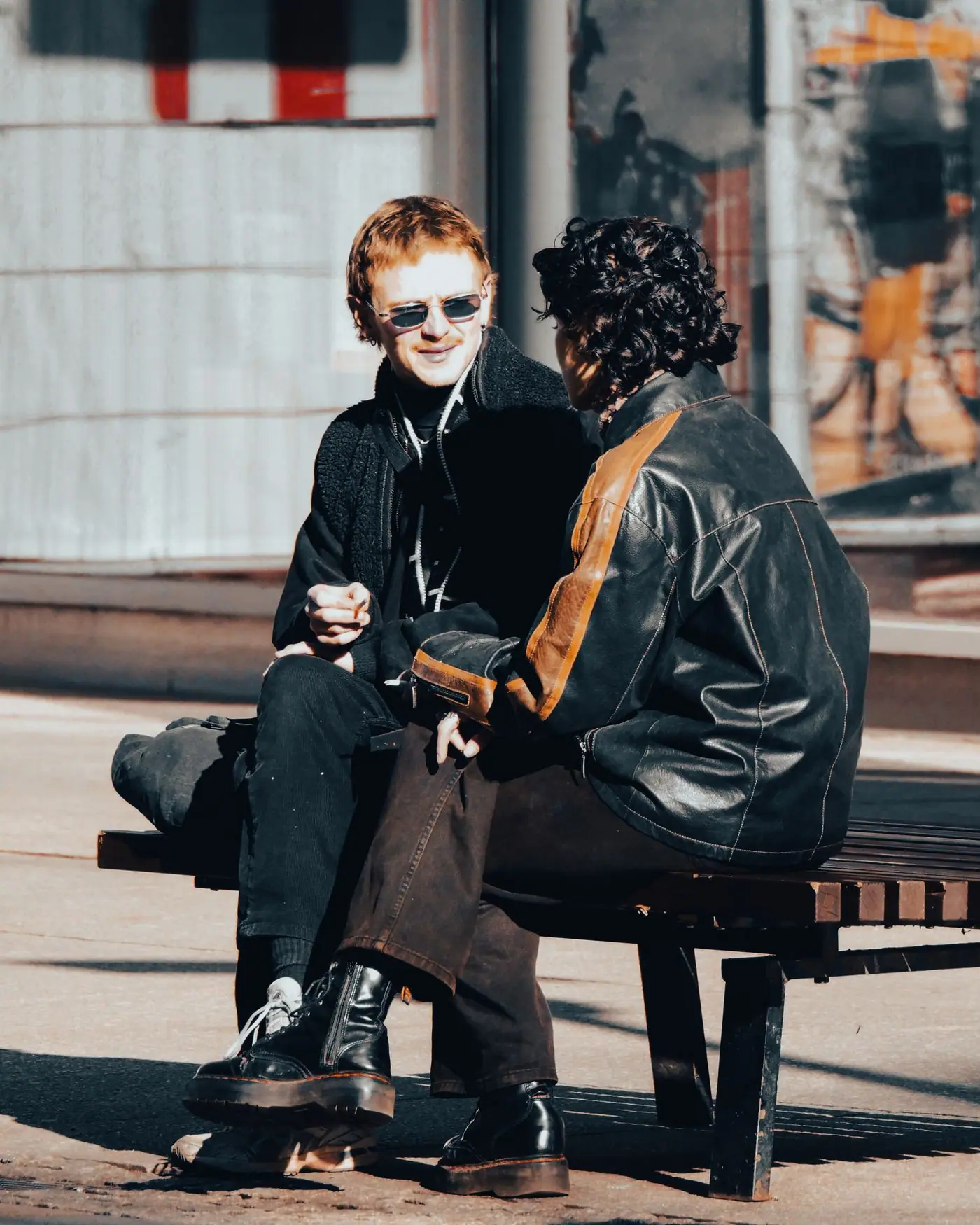 Two friends talking on a bench in a sunny urban setting.