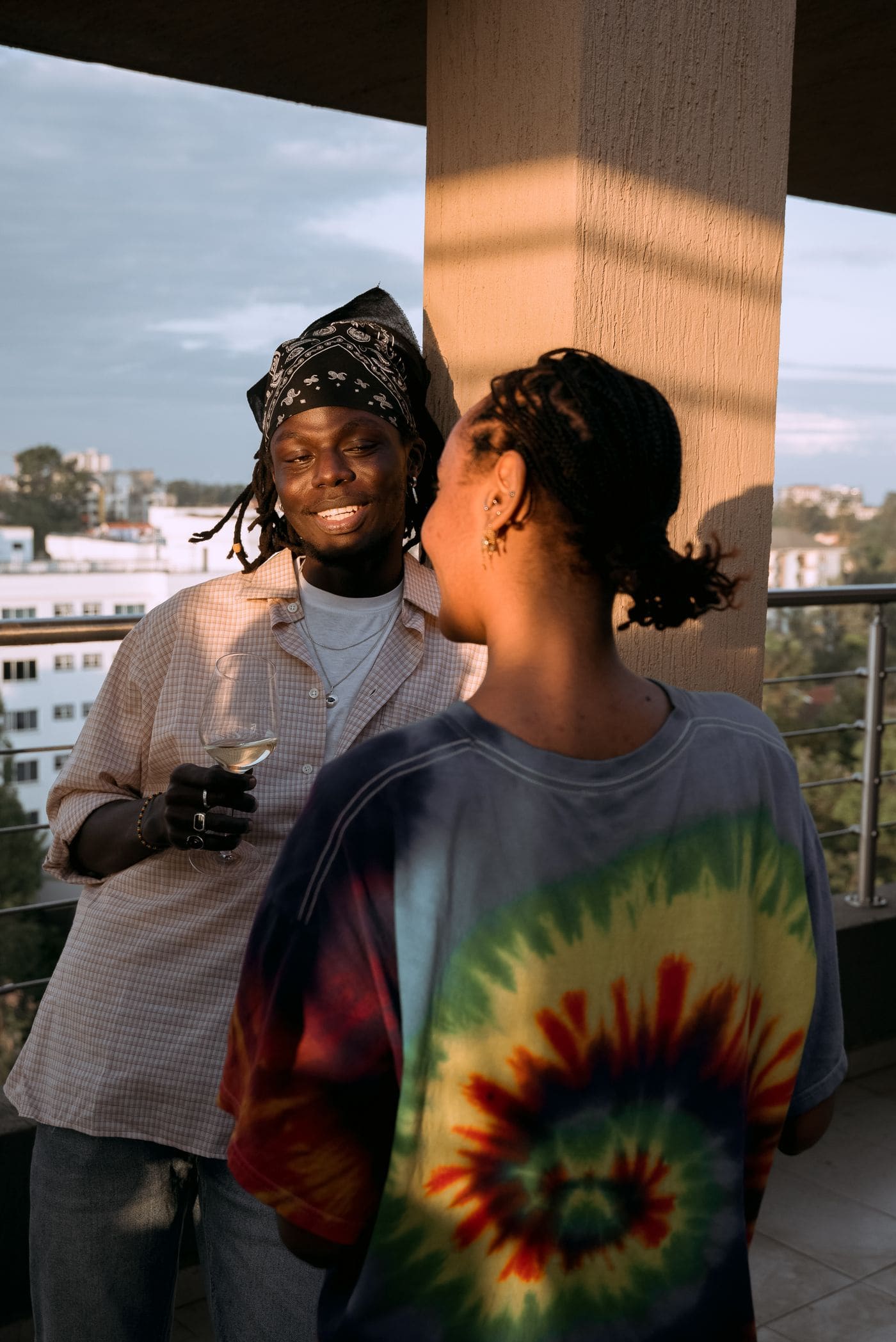 Two friends talking with drinks on a balcony at sunset.