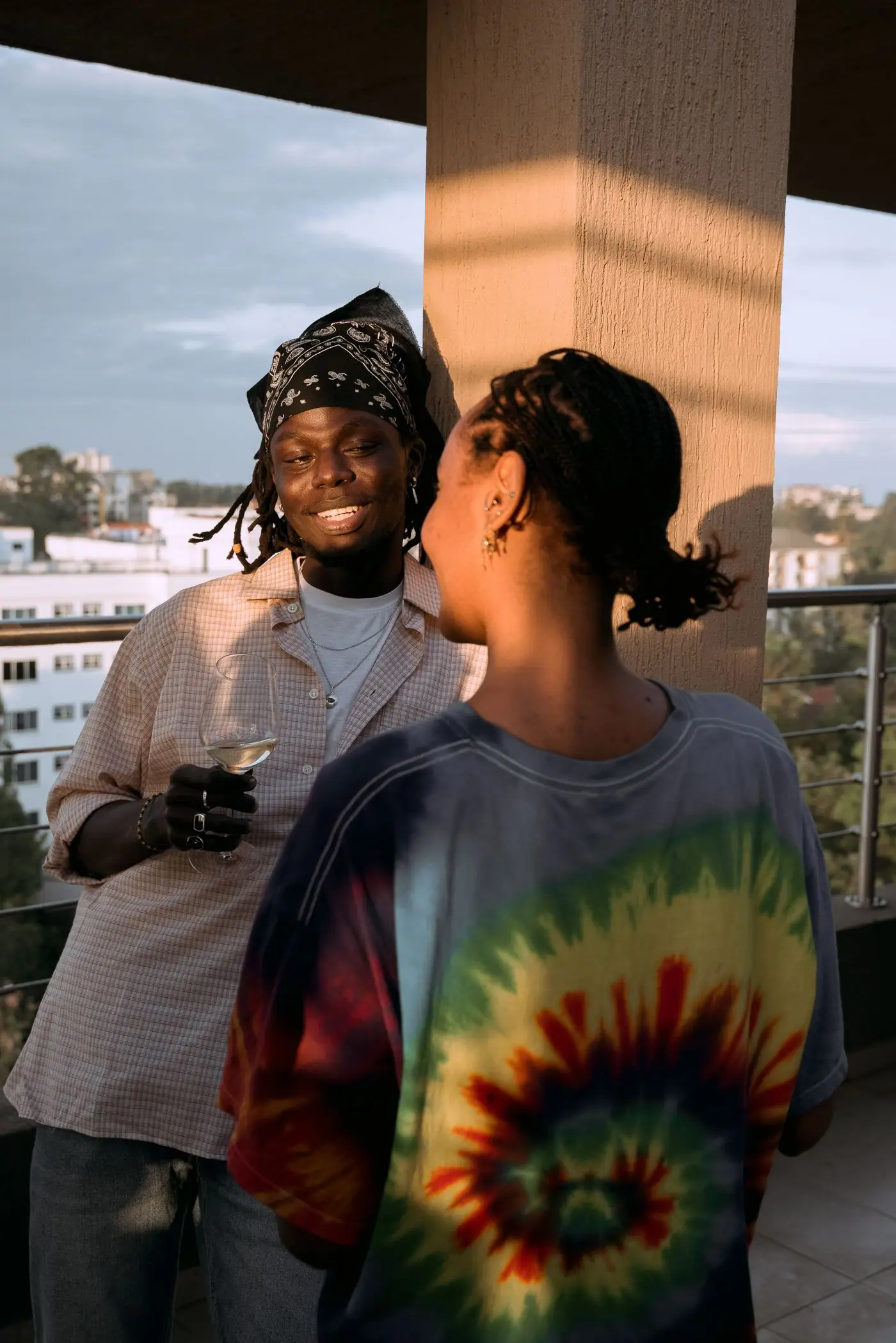 Two friends talking with drinks on a balcony at sunset.