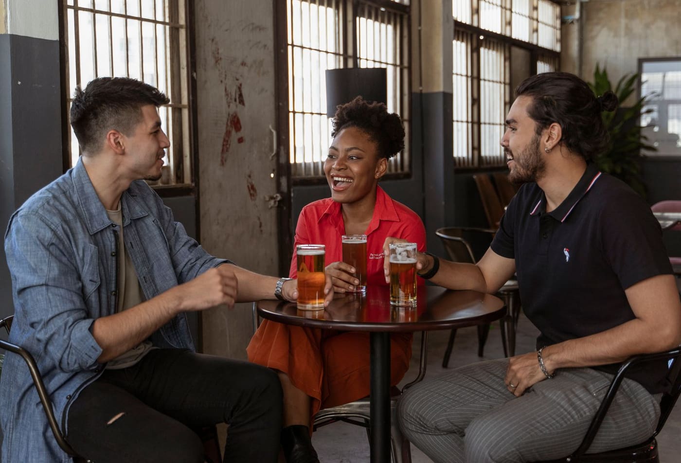 Three friends laughing together over beers at a cozy pub table.