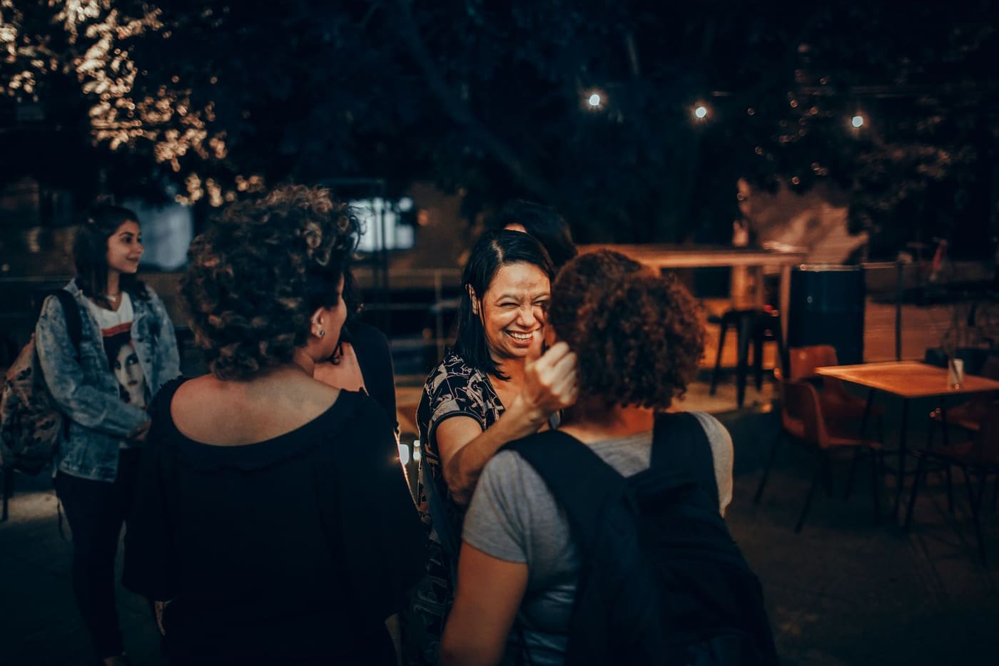 Friends sharing laughter at an outdoor cafe under warm evening lights.