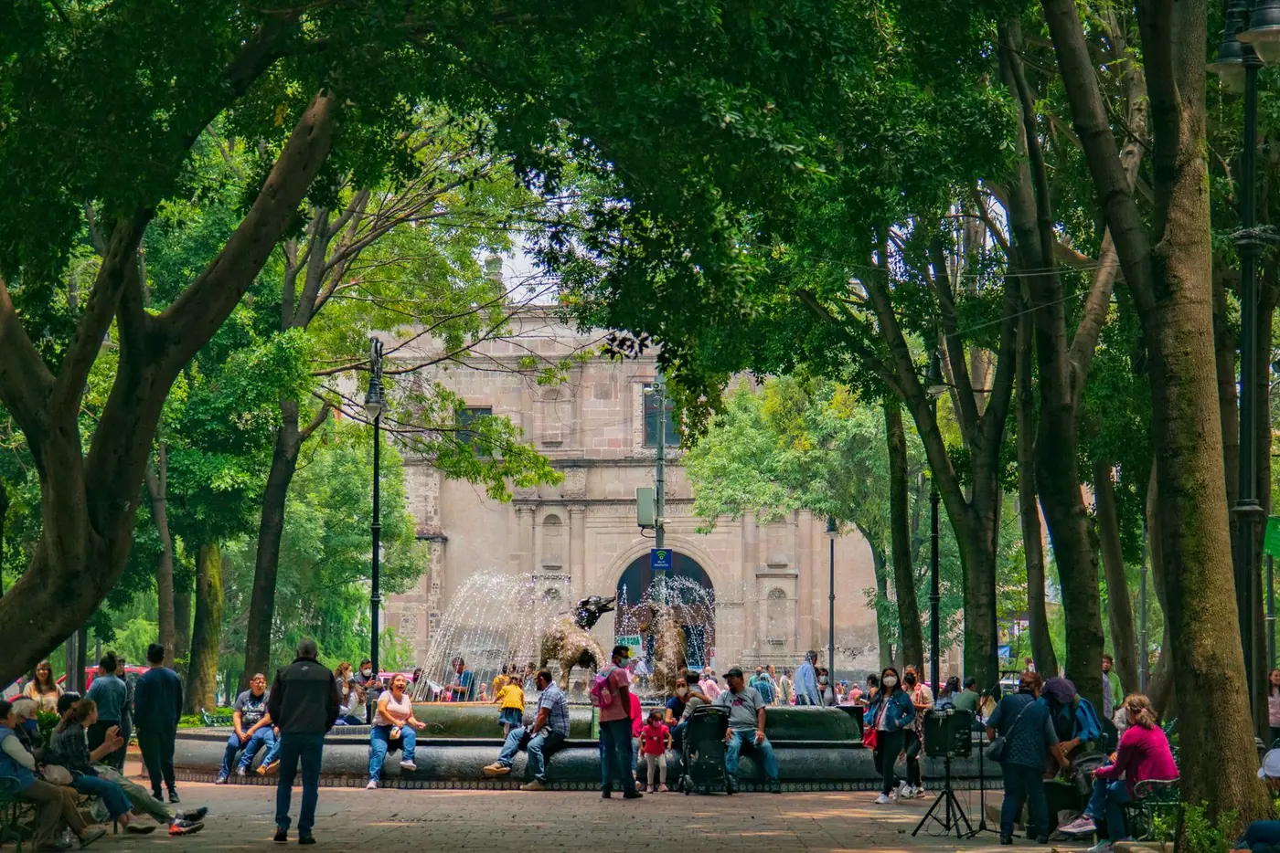 People sitting around a fountain in a tree-lined park in Mexico City.