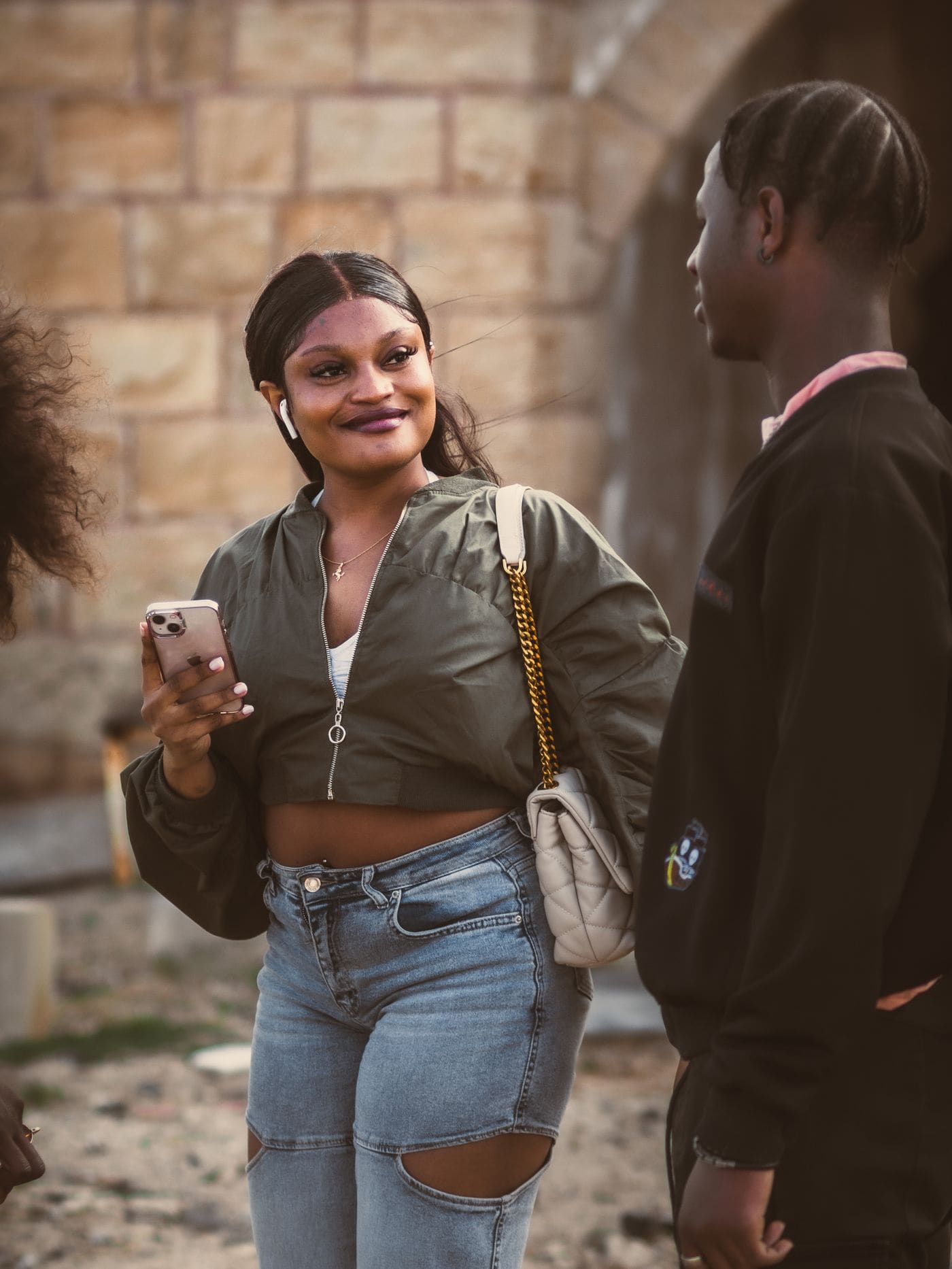 A group of friends having a casual conversation outdoors while one holds a phone.