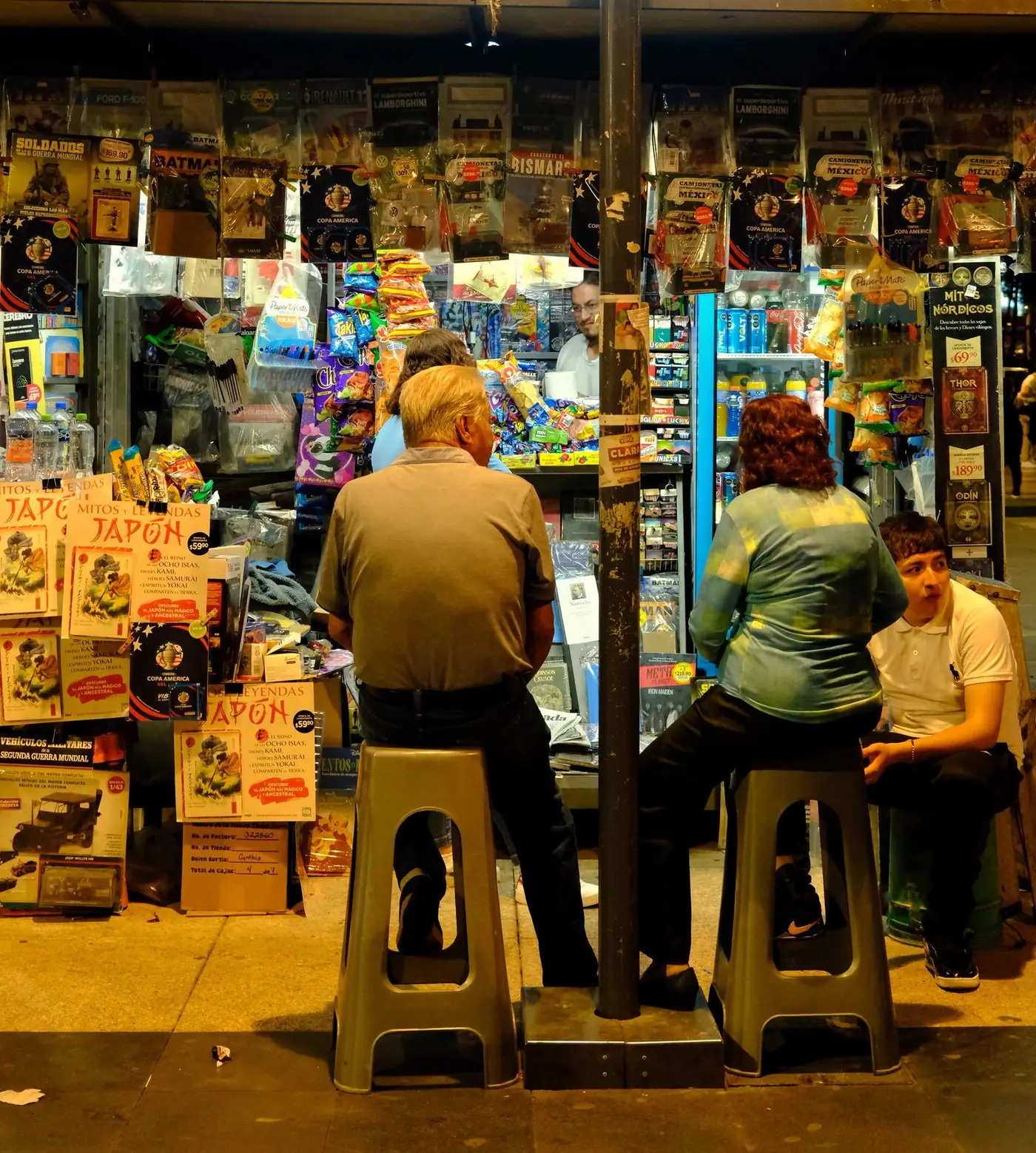 People sitting at a newsstand in Mexico City at night.
