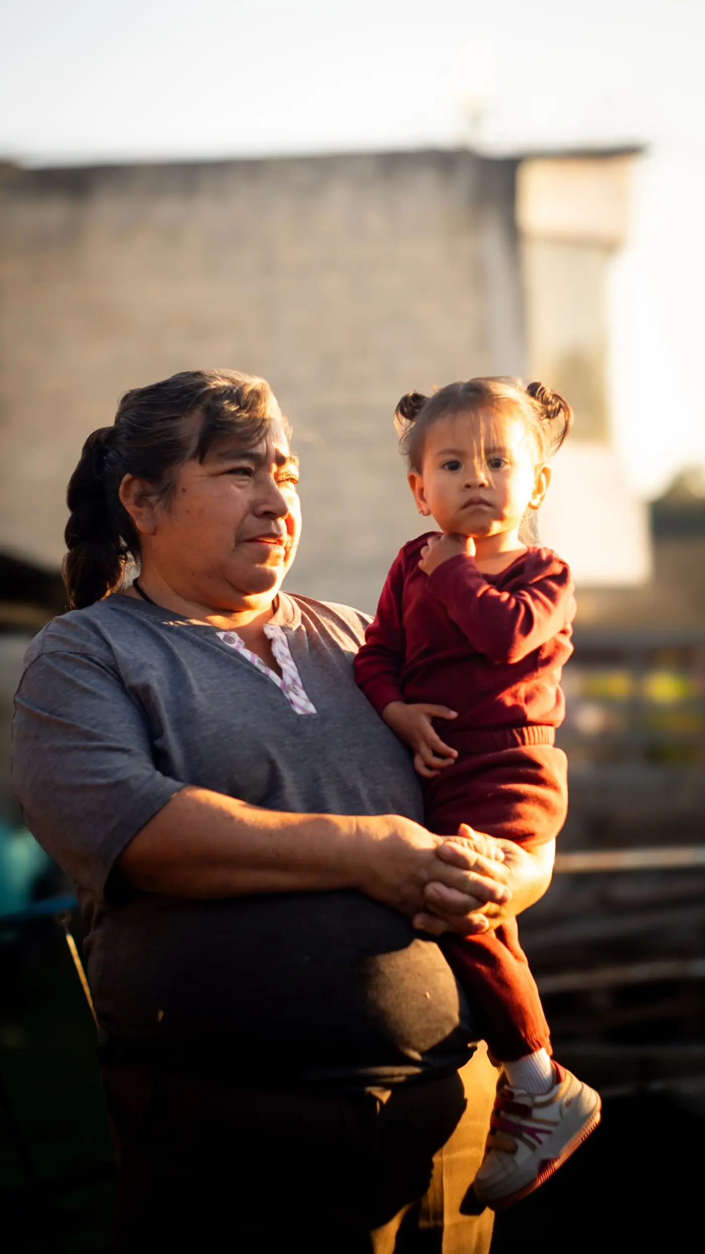 A grandmother holding a small child in her arms outdoors at golden hour.