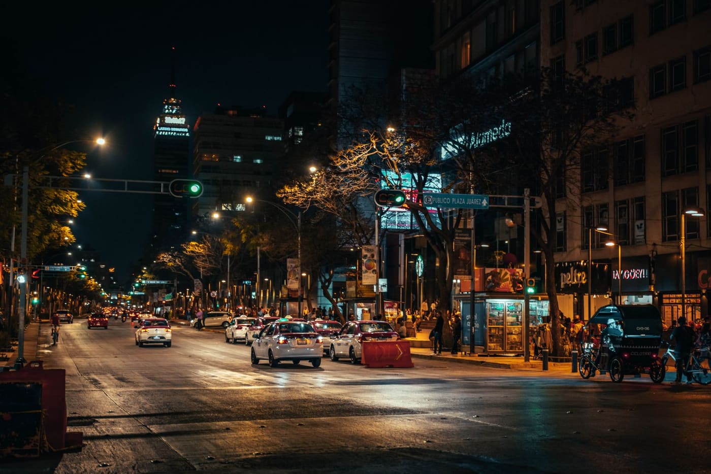 Busy Mexico City street at night with storefronts and cars.
