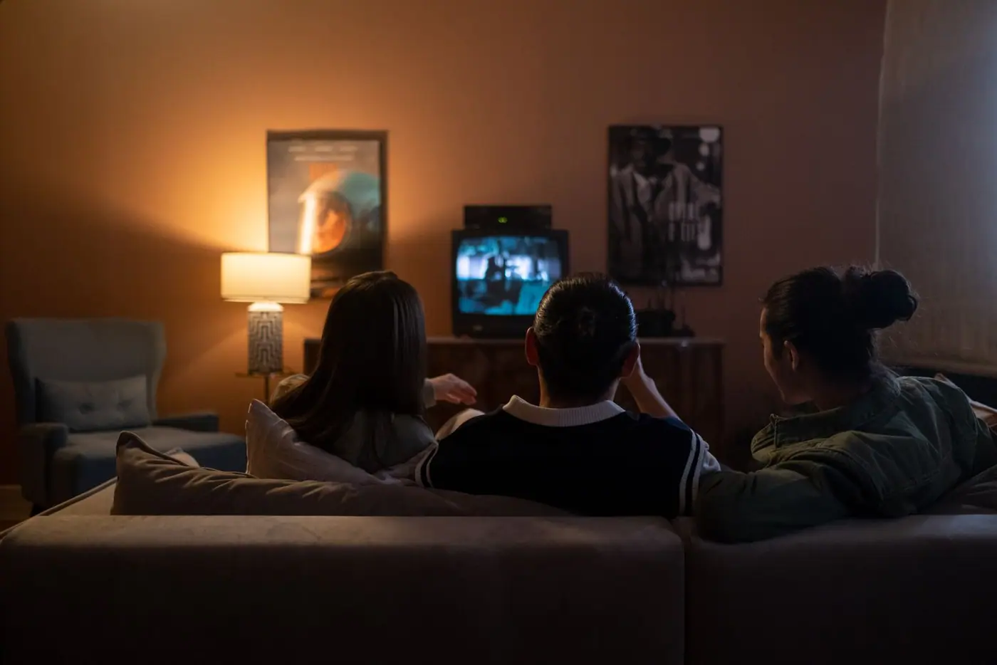 Three friends sitting on a couch watching something on television.