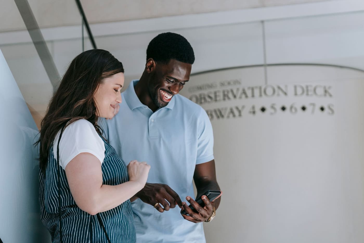 Two friends laughing together while looking at a smartphone.