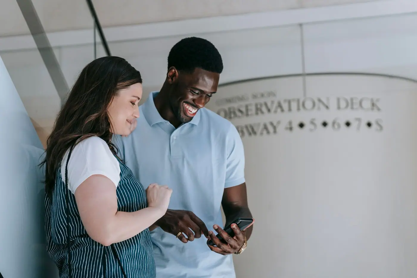 Two friends laughing together while looking at a smartphone.