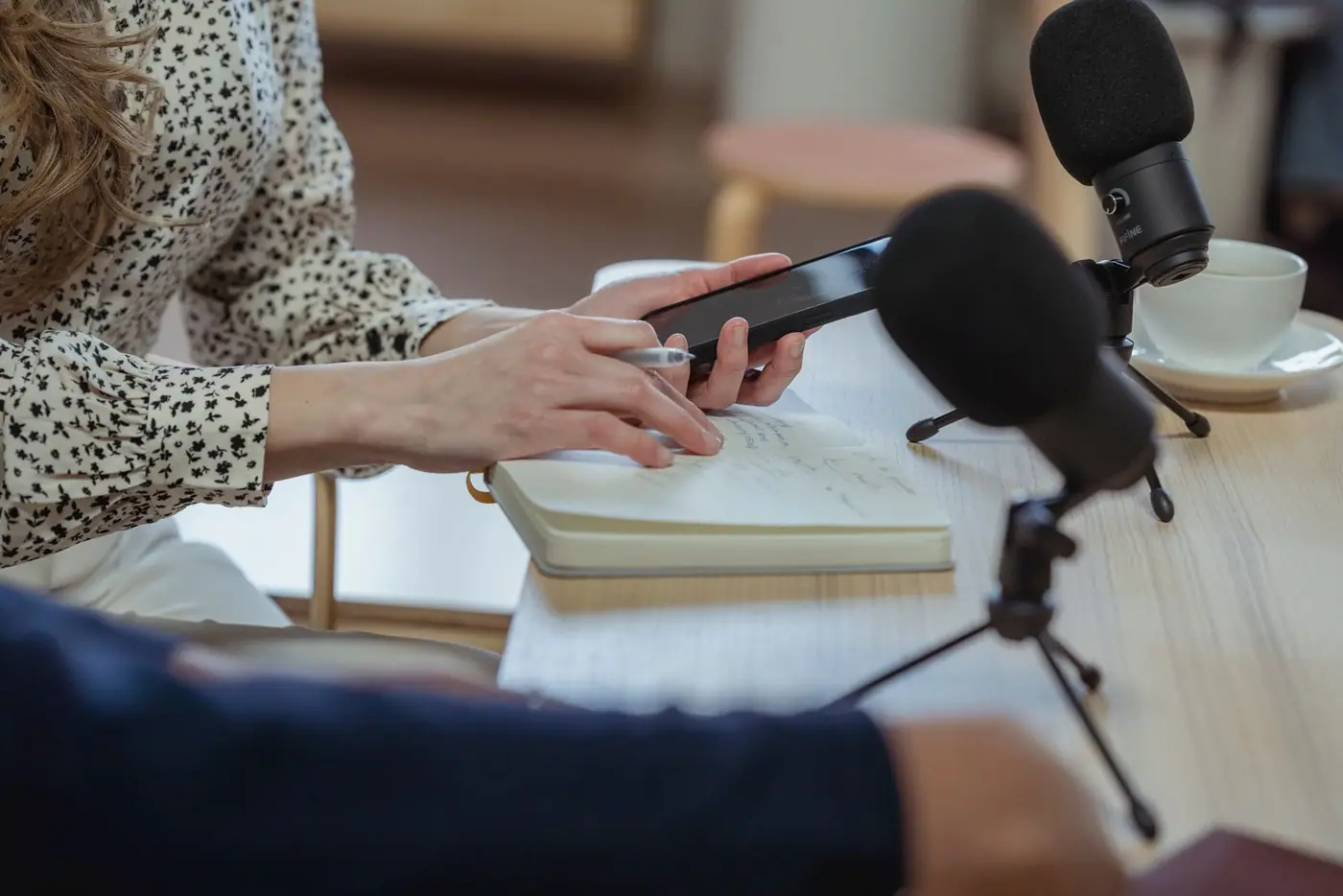 A person using a phone beside a notebook and microphone at a cafe table.