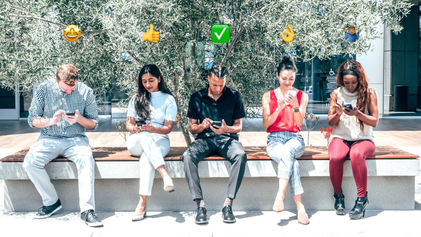A diverse group of friends sitting outdoors and looking at smartphones beneath emoji graphics.