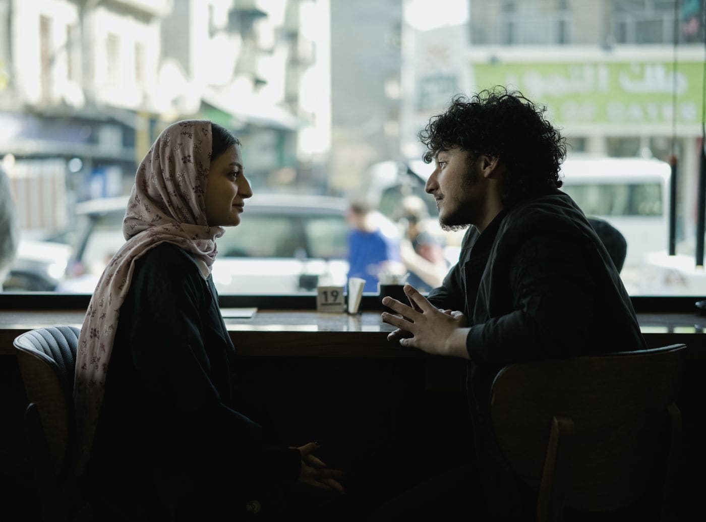 Two people silhouetted while talking across a cafe table.