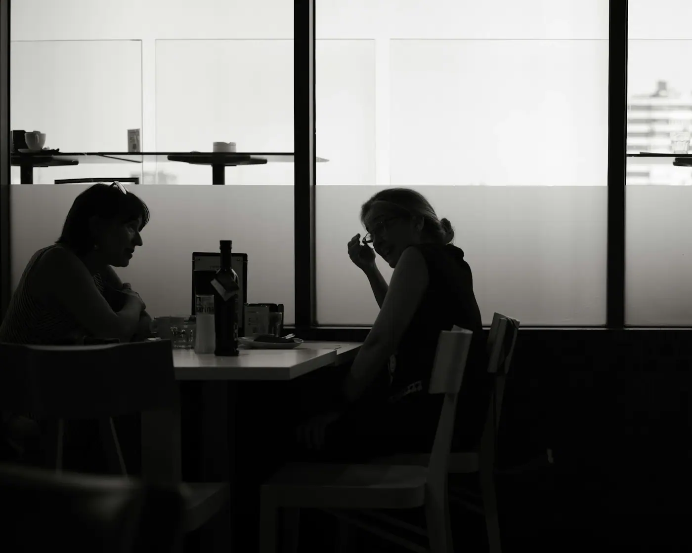 Two people sitting in silhouette at a table in a dimly lit room.