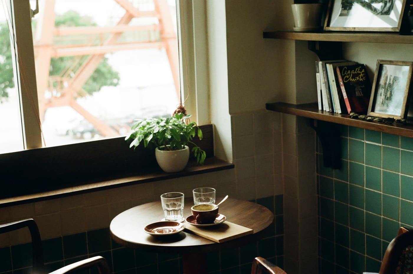 Two glasses of coffee on a small table by a window, with a plant and a record shelf behind.