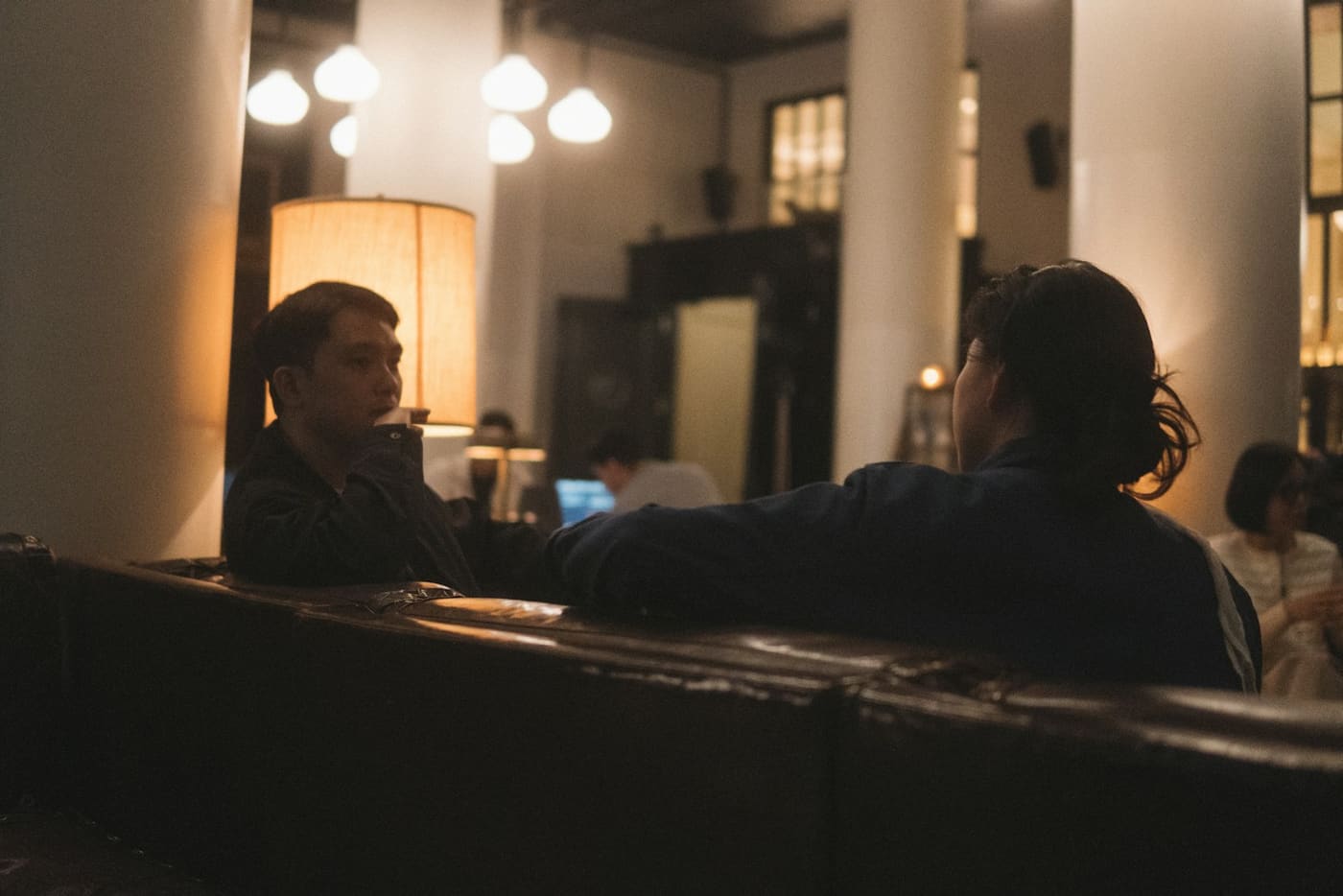 Two people leaning in to talk to each other across a dimly lit bar.