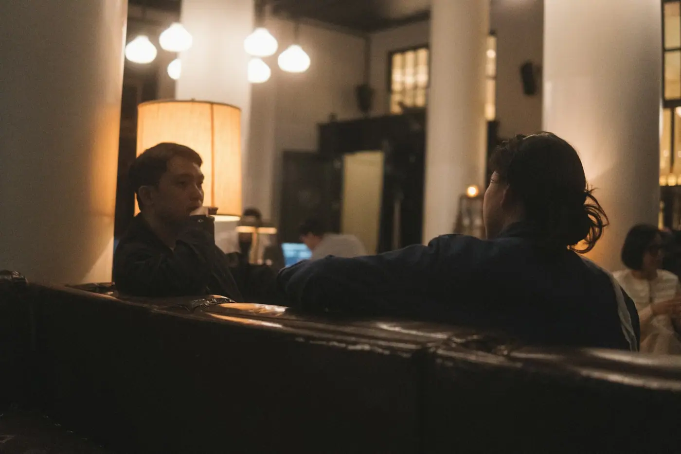 Two people leaning in to talk to each other across a dimly lit bar.