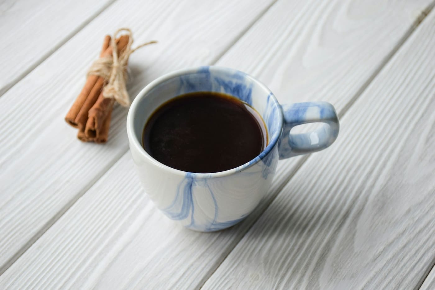 A cup of coffee beside cinnamon sticks on a wooden surface.
