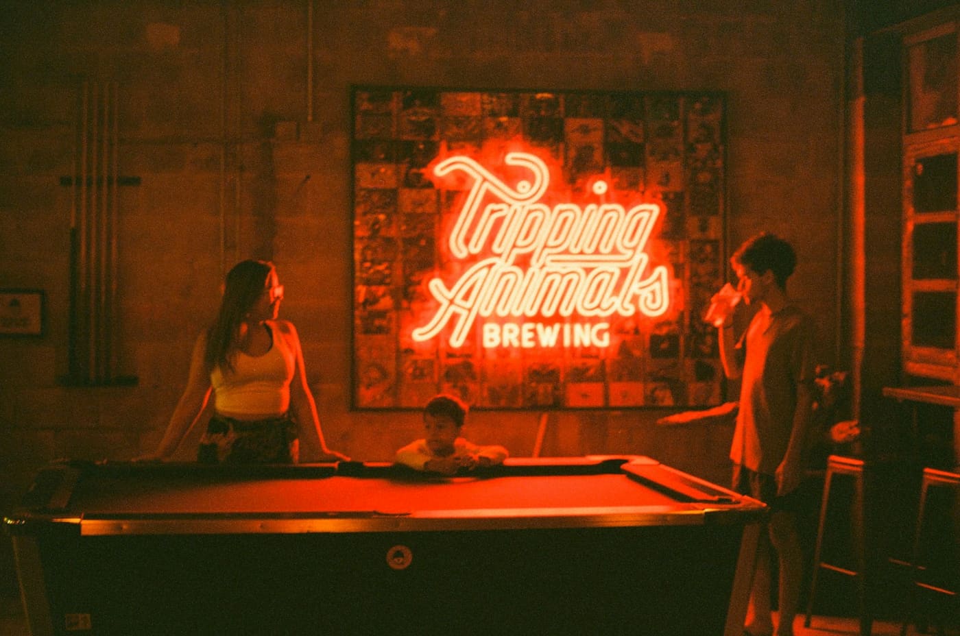 People playing pool under a neon sign inside a bar.