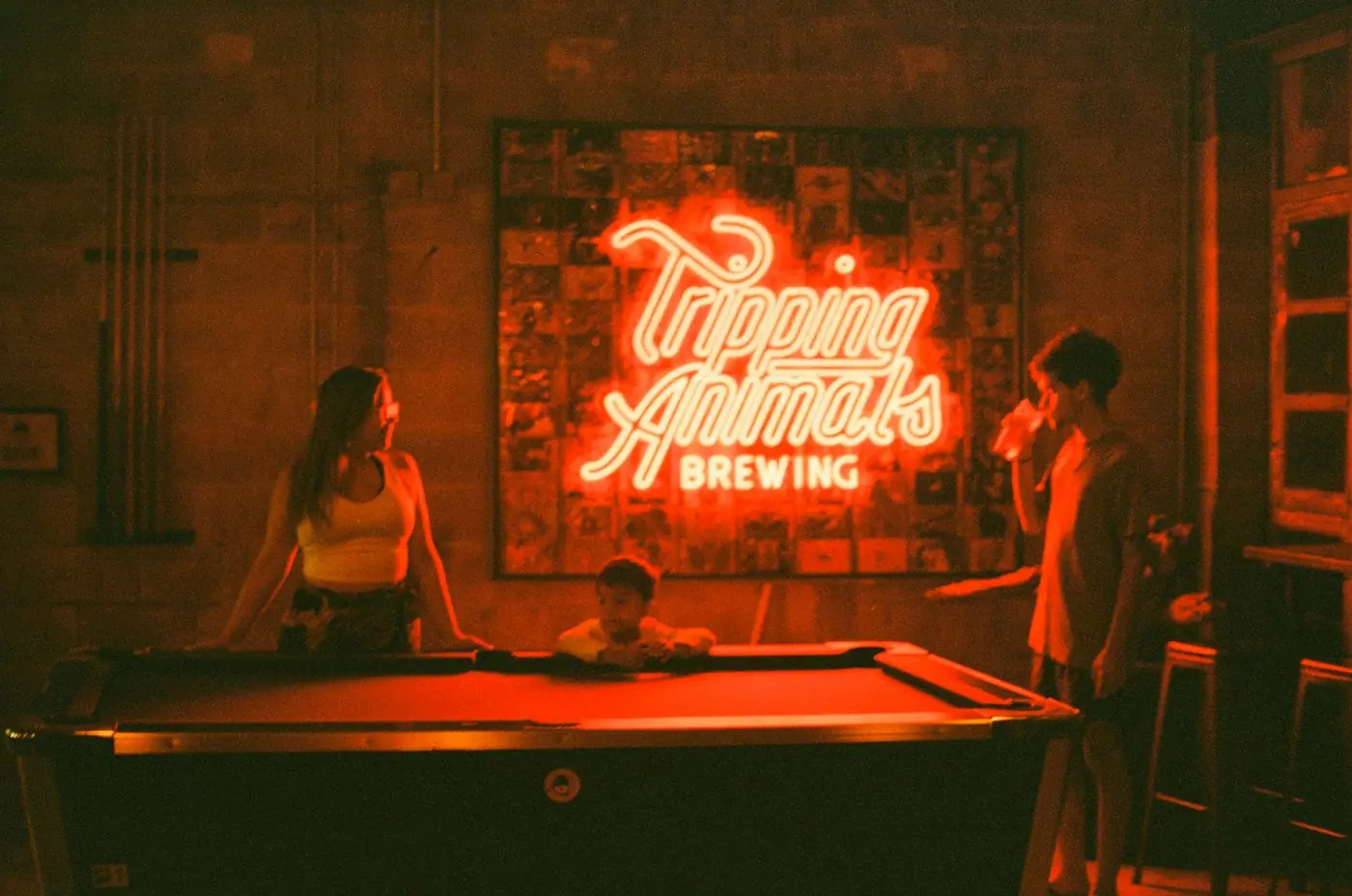 People playing pool under a neon sign inside a bar.