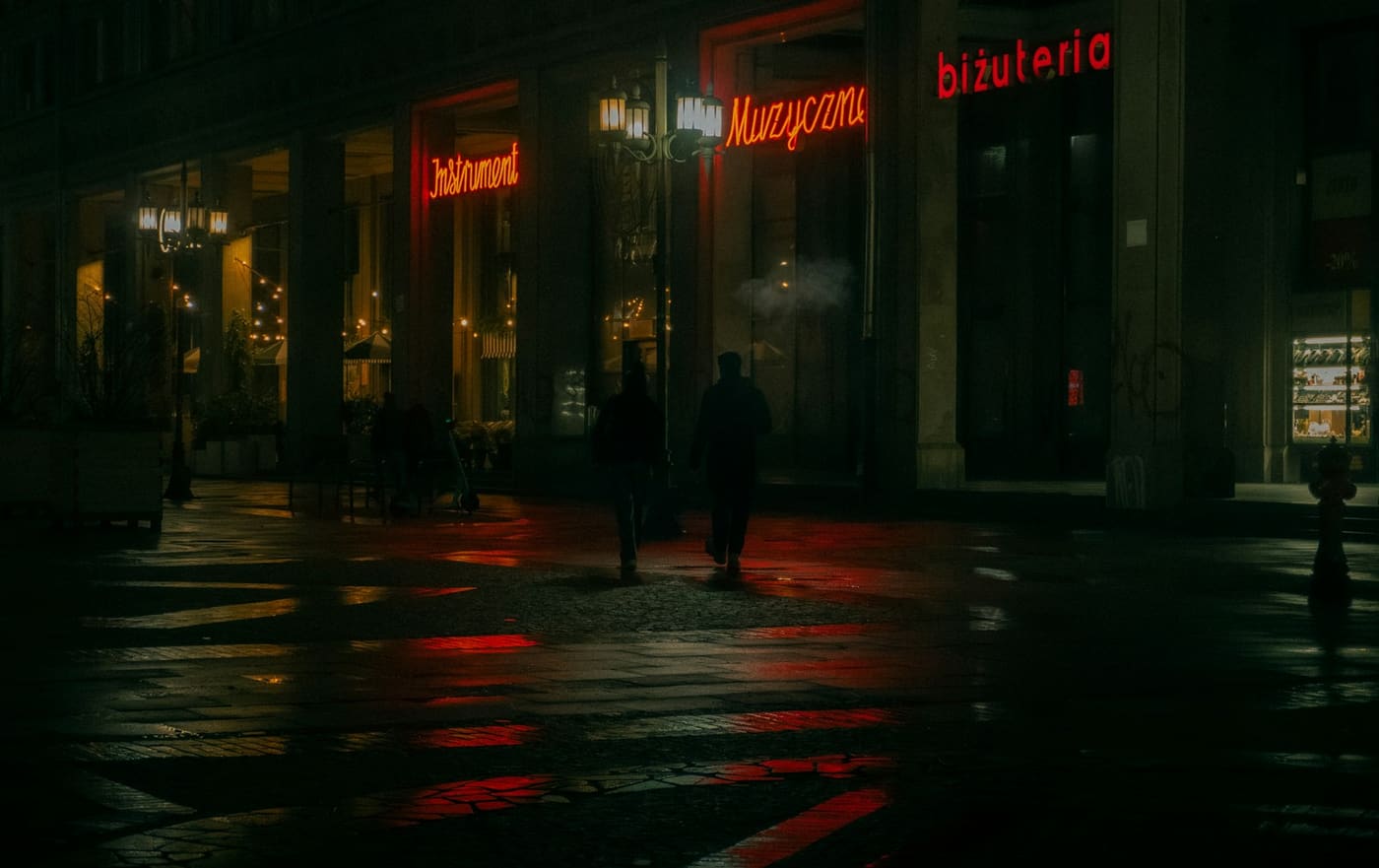 People walking along a wet city street at night.