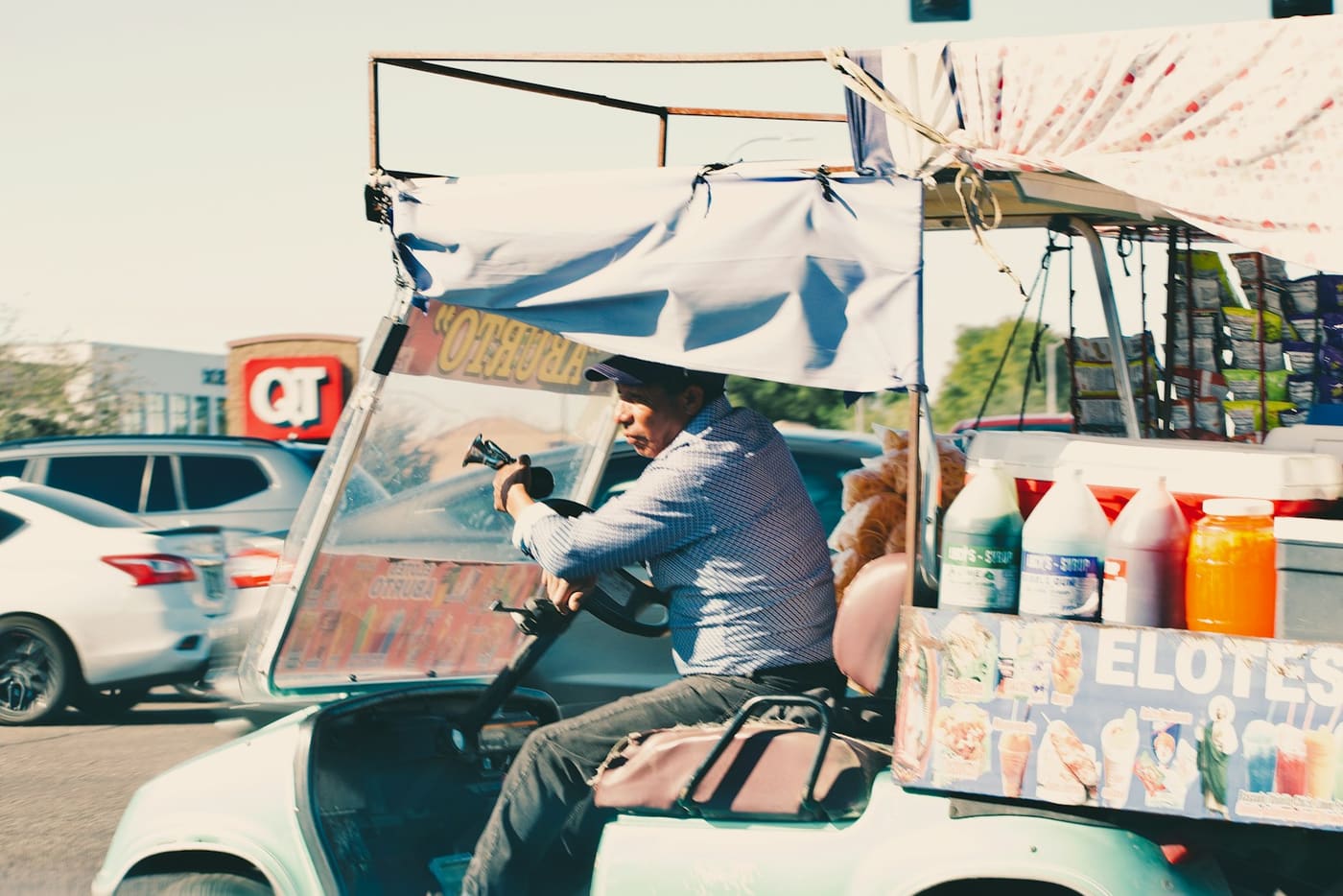 A vendor riding a motorised elote cart stacked with bottles and drinks.