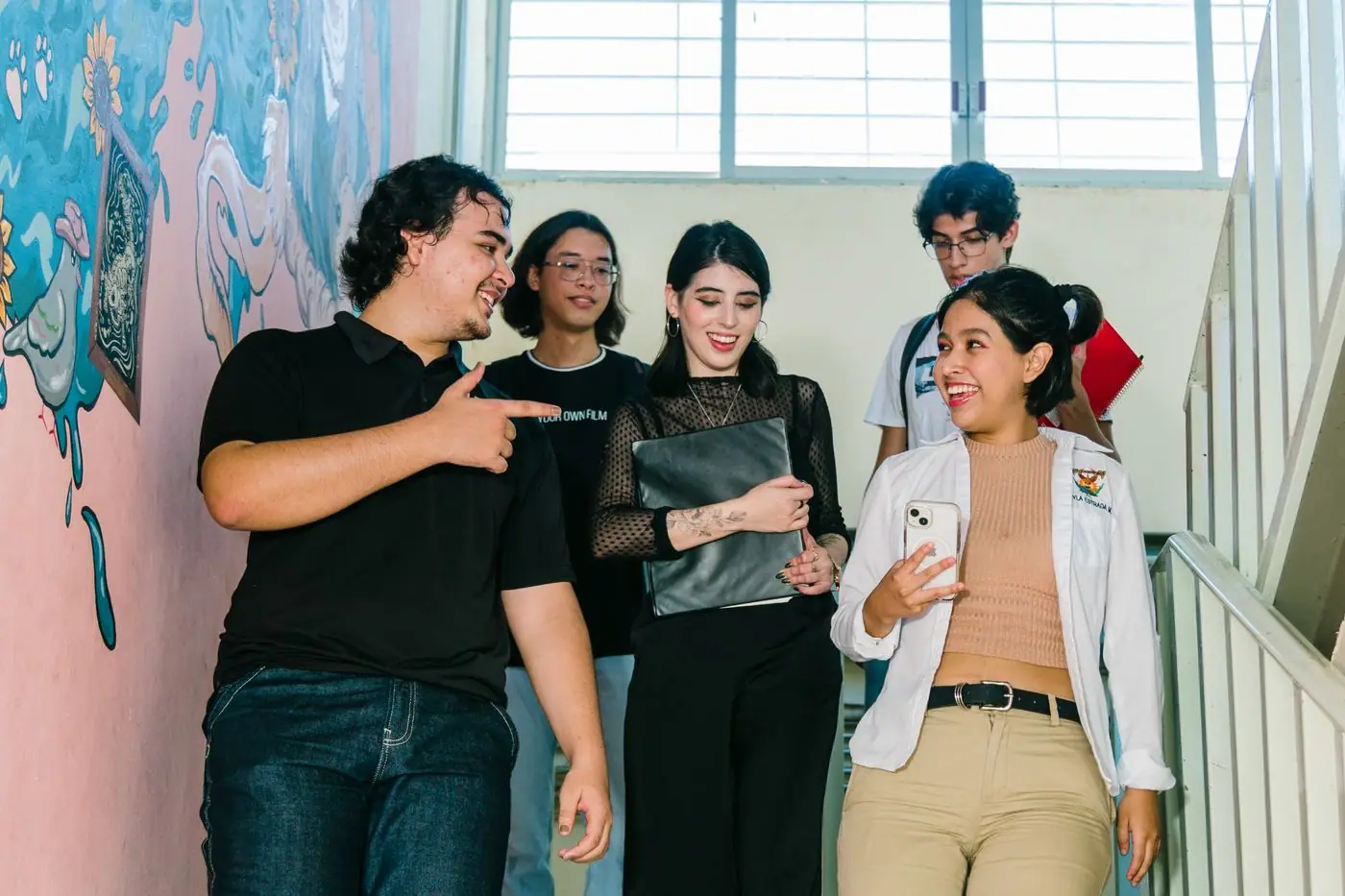 A group of young people standing on a staircase in front of a painted mural.