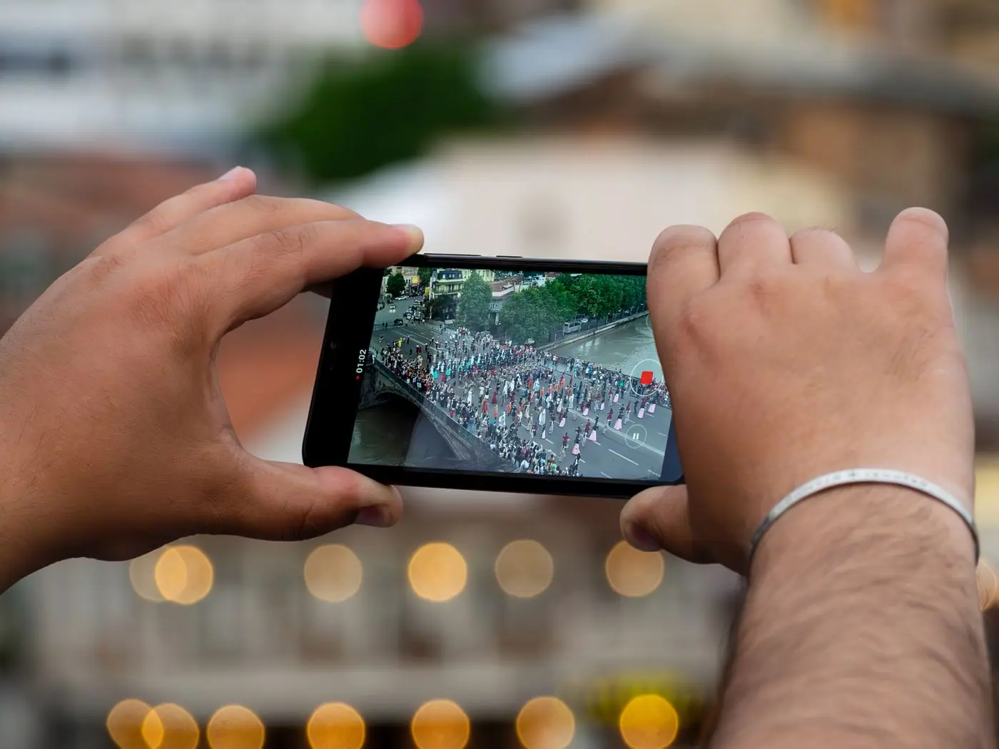 Two hands holding a phone up to photograph a lit scene at night.