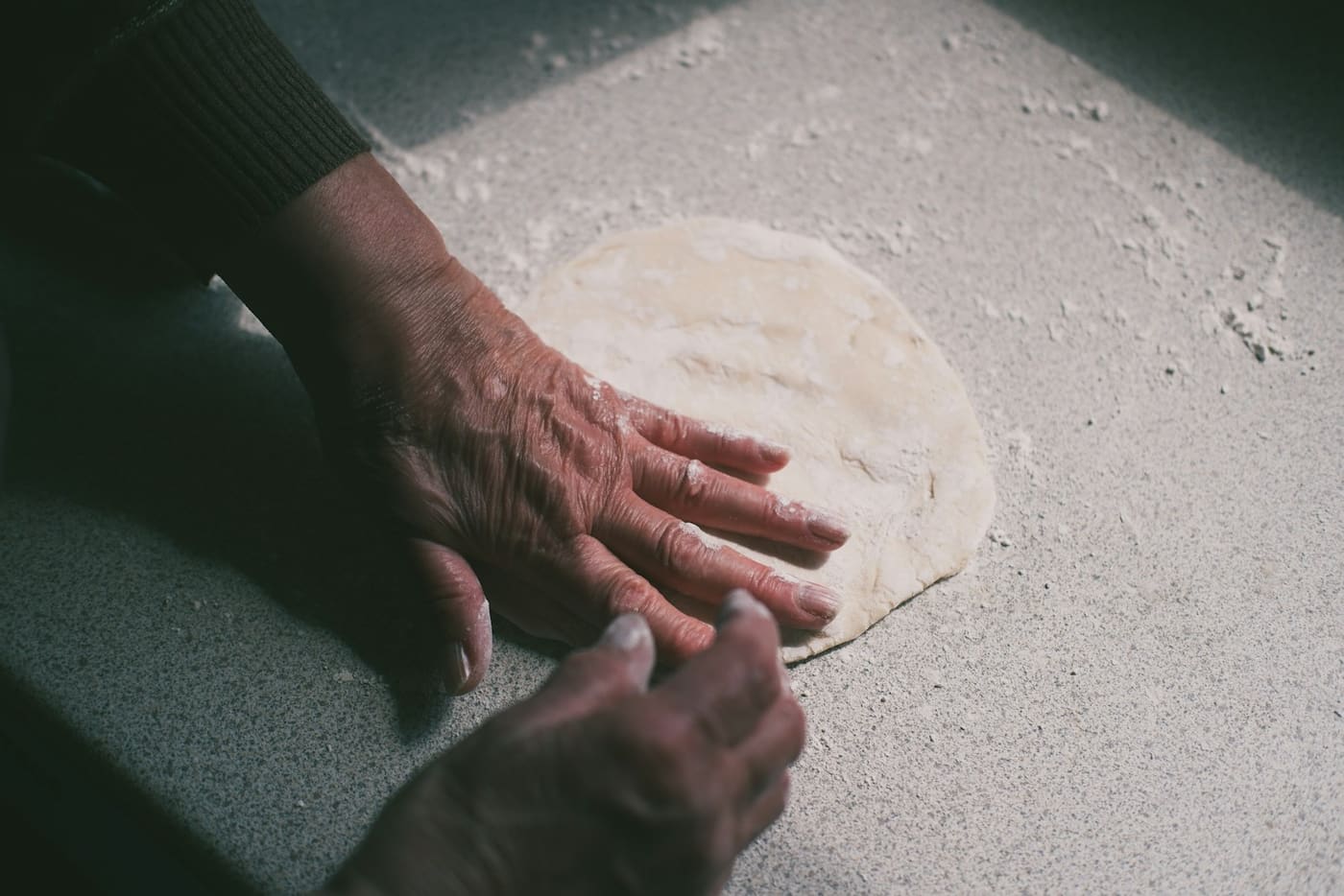 Hands pressing and working a ball of dough on a floured surface.