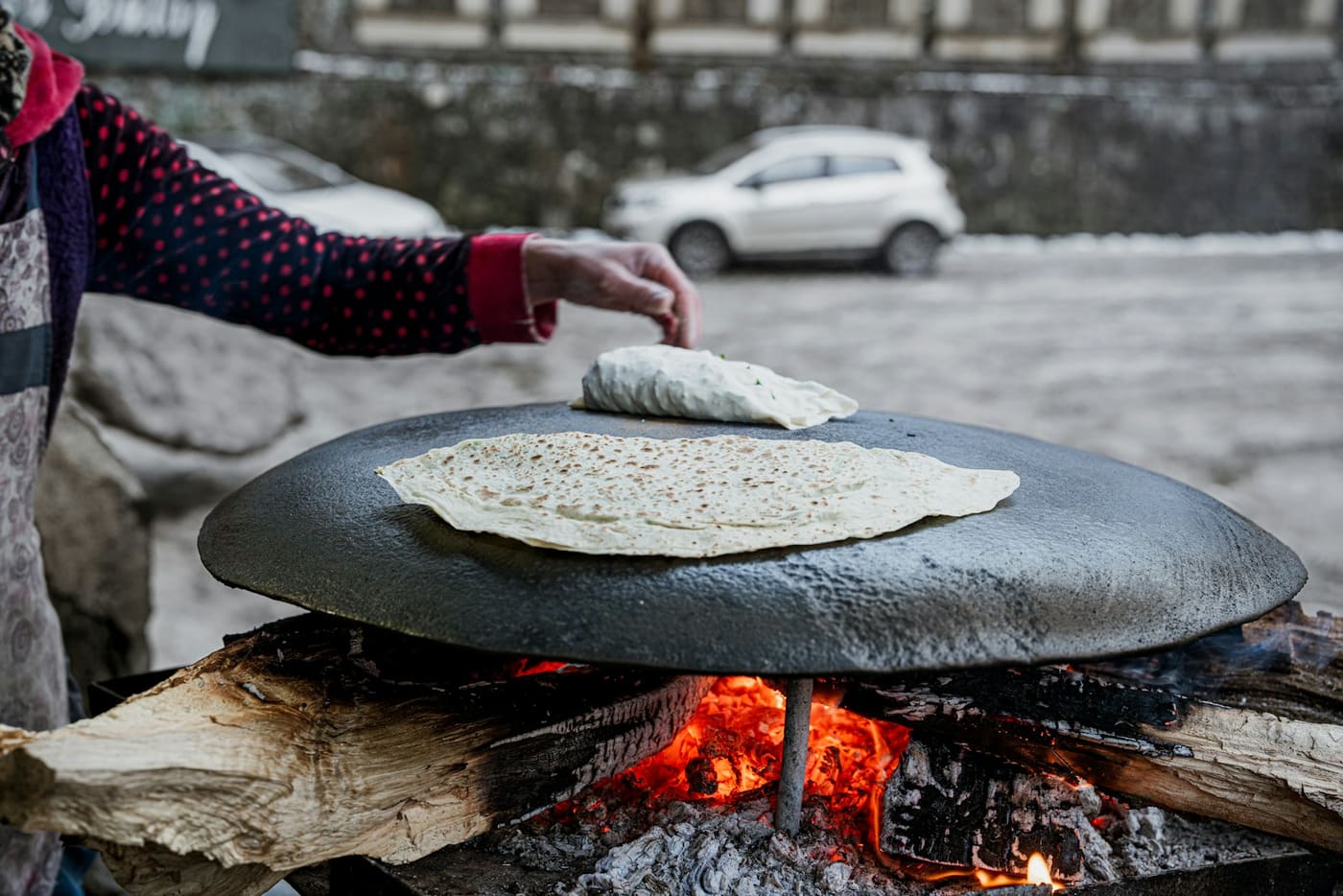 A flatbread cooking on a hot round griddle over an open fire.