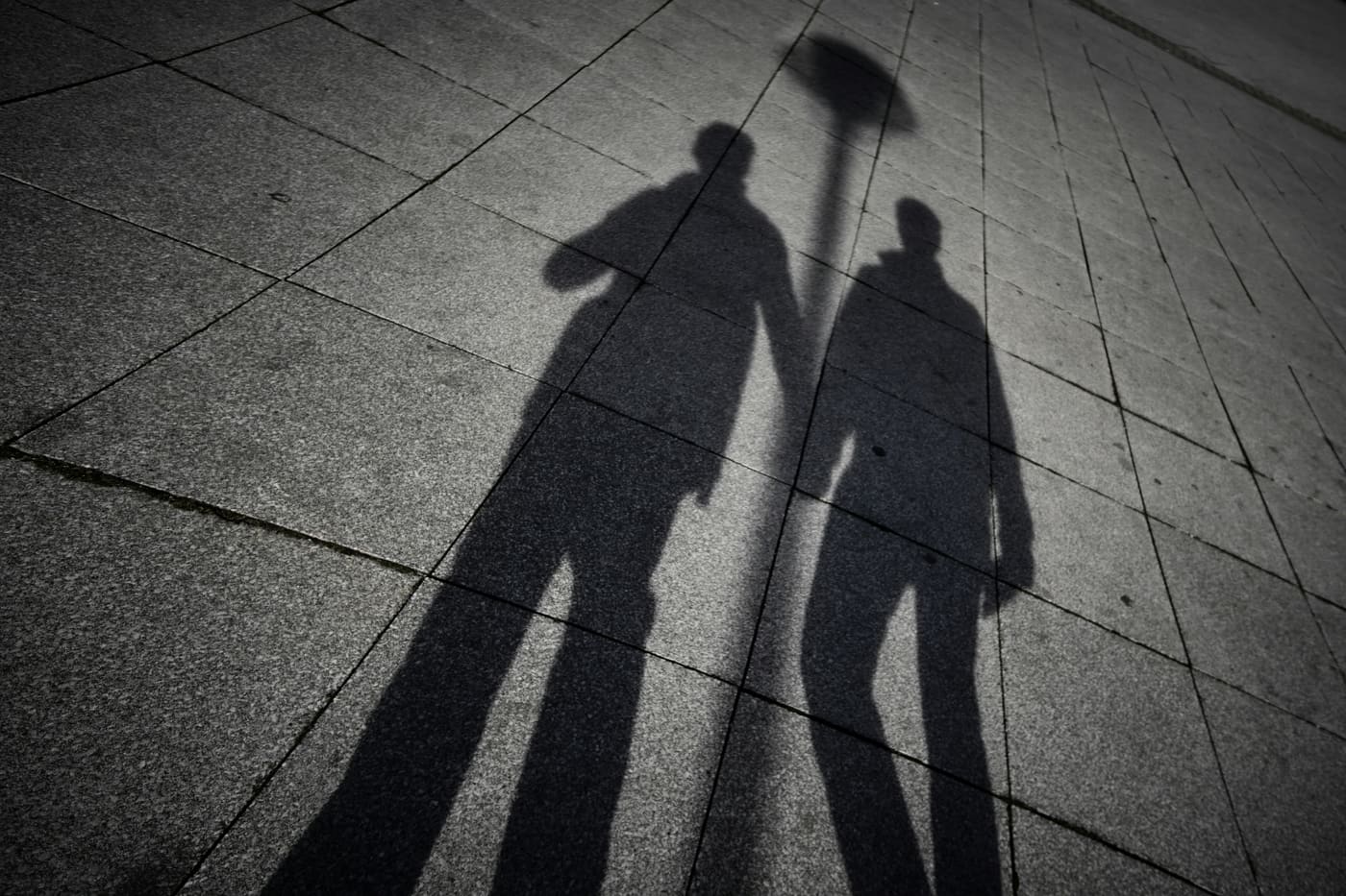 The shadows of two men holding hands on pavement.