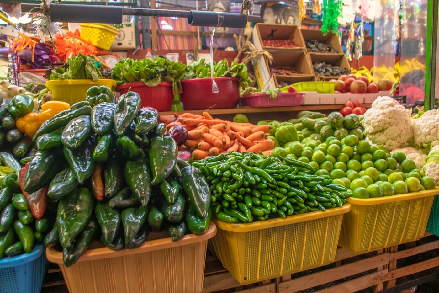 A Mexican market stall stacked with dried chillies, fresh limes, and vegetables in crates.