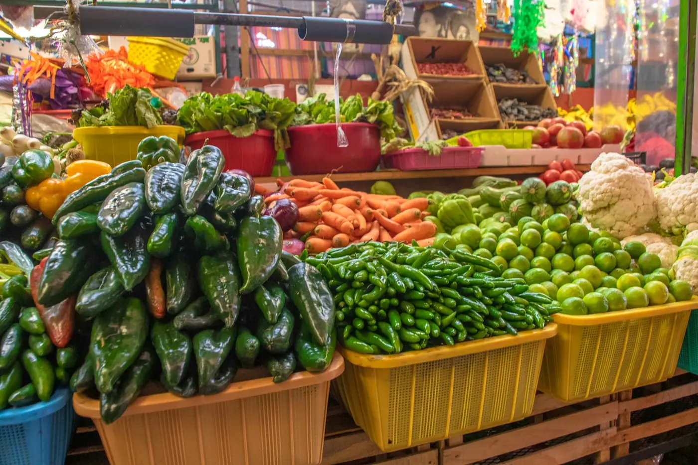A Mexican market stall stacked with dried chillies, fresh limes, and vegetables in crates.