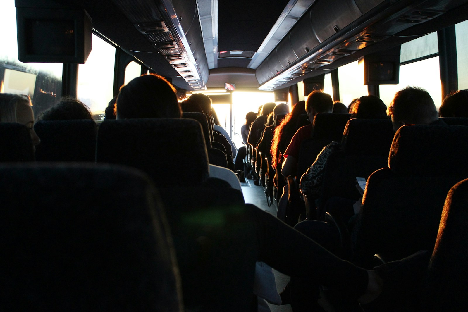 Passengers standing and sitting inside a bus, silhouetted against bright windows.