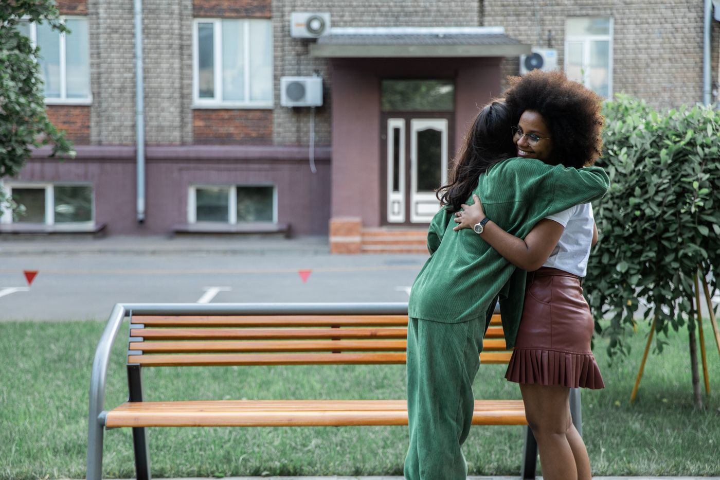 Two friends smiling during a greeting beside a city bench.