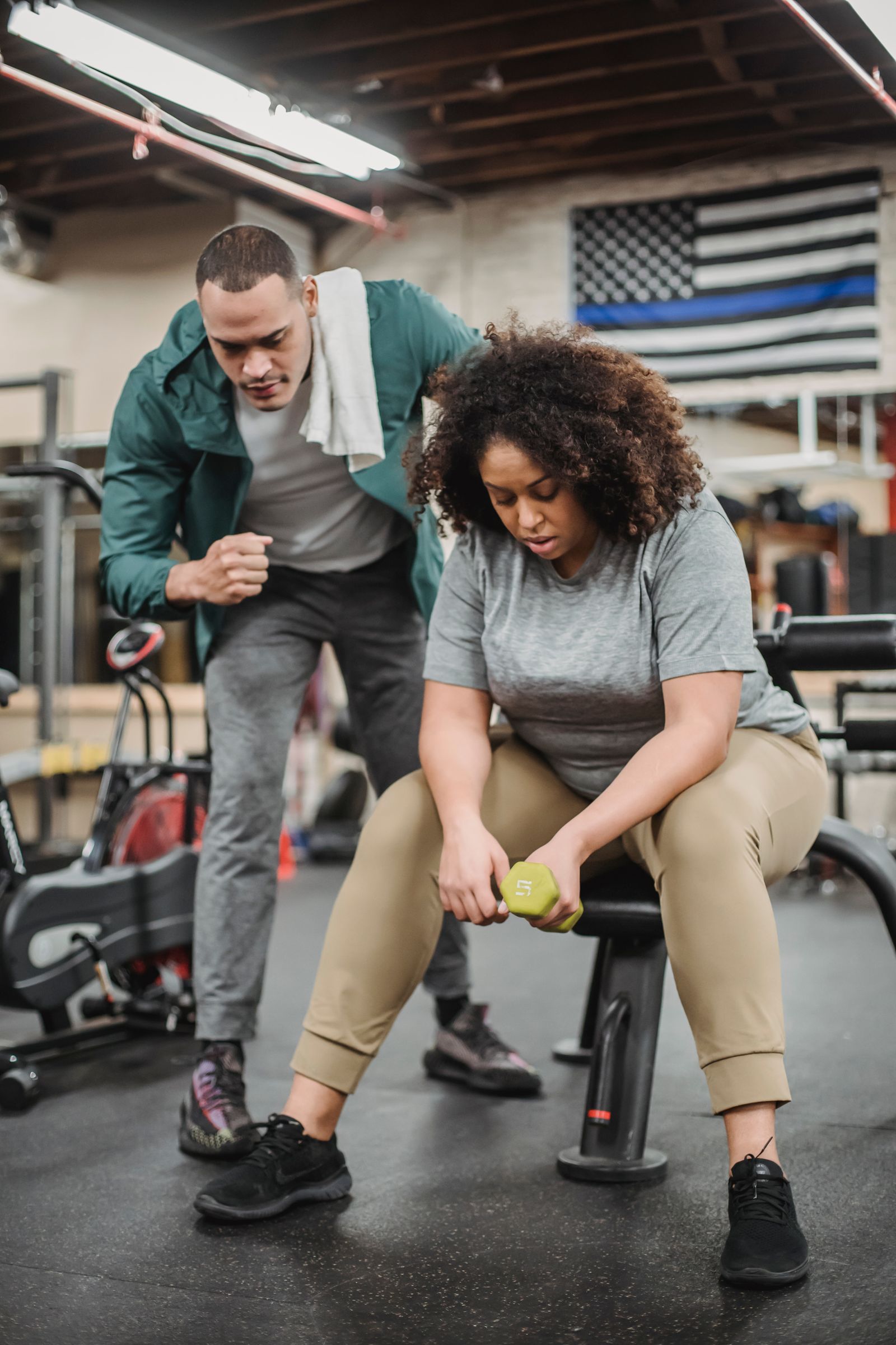 A personal trainer helping an adult exercise safely with a dumbbell.