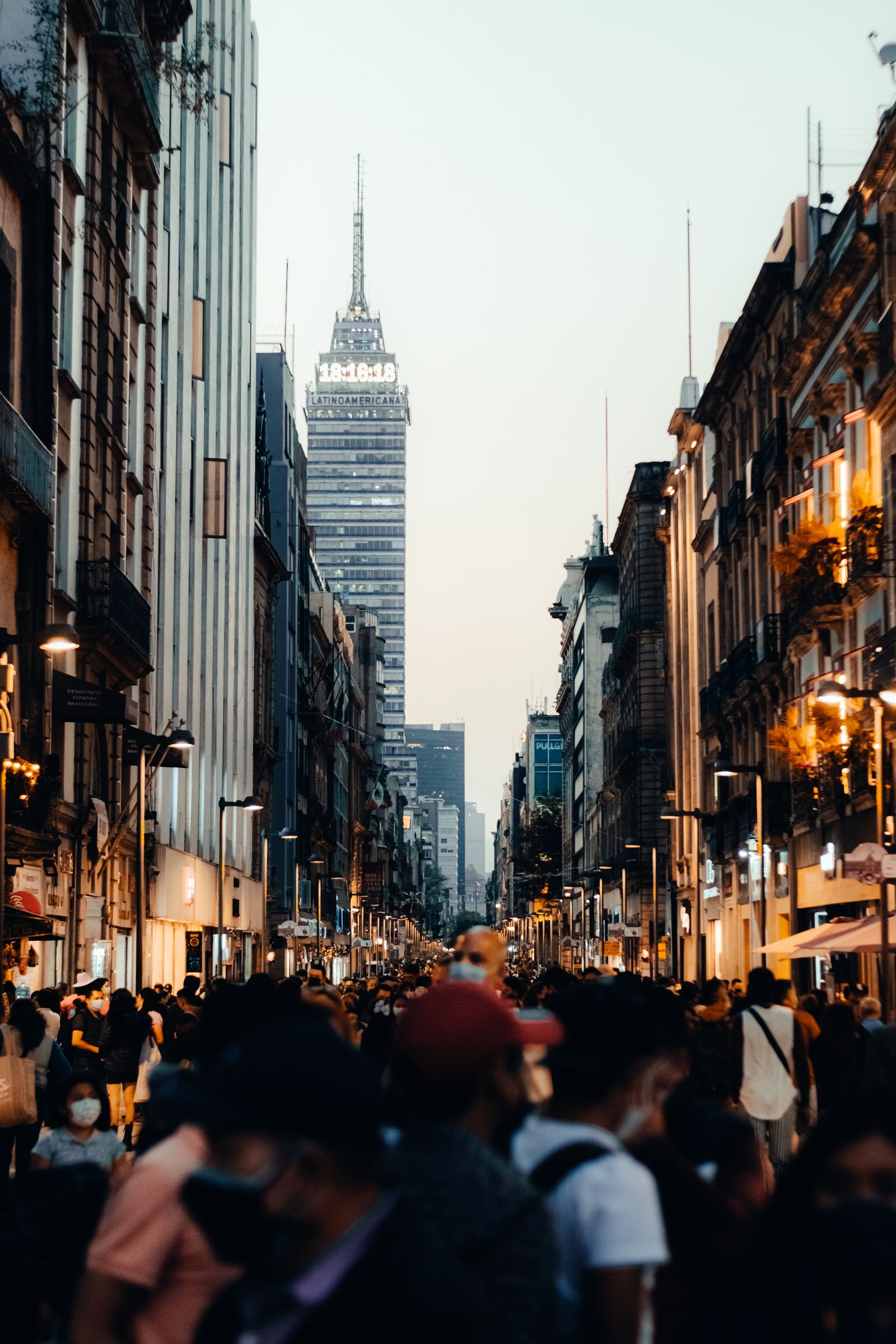 A crowded Mexico City street with Torre Latinoamericana at dusk.