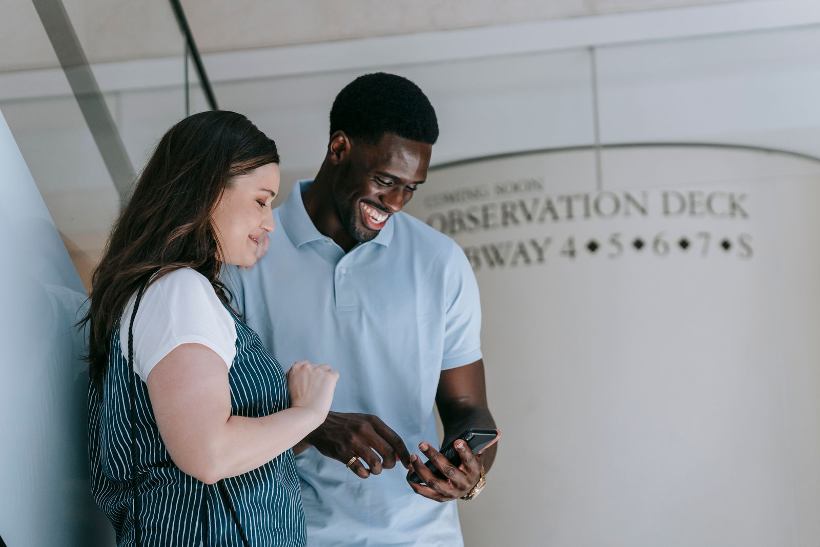 Two friends laughing together while looking at a smartphone.