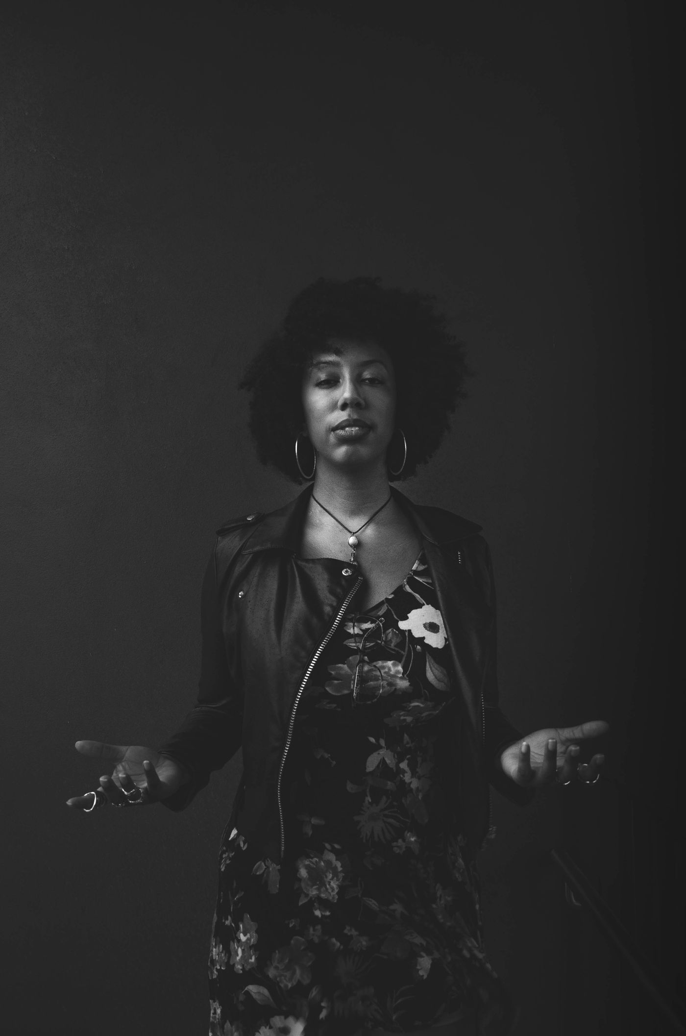 A woman shrugging with open hands against a dark background.