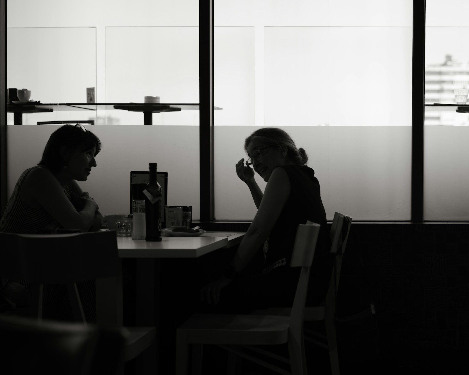 Two people sitting in silhouette at a table in a dimly lit room.