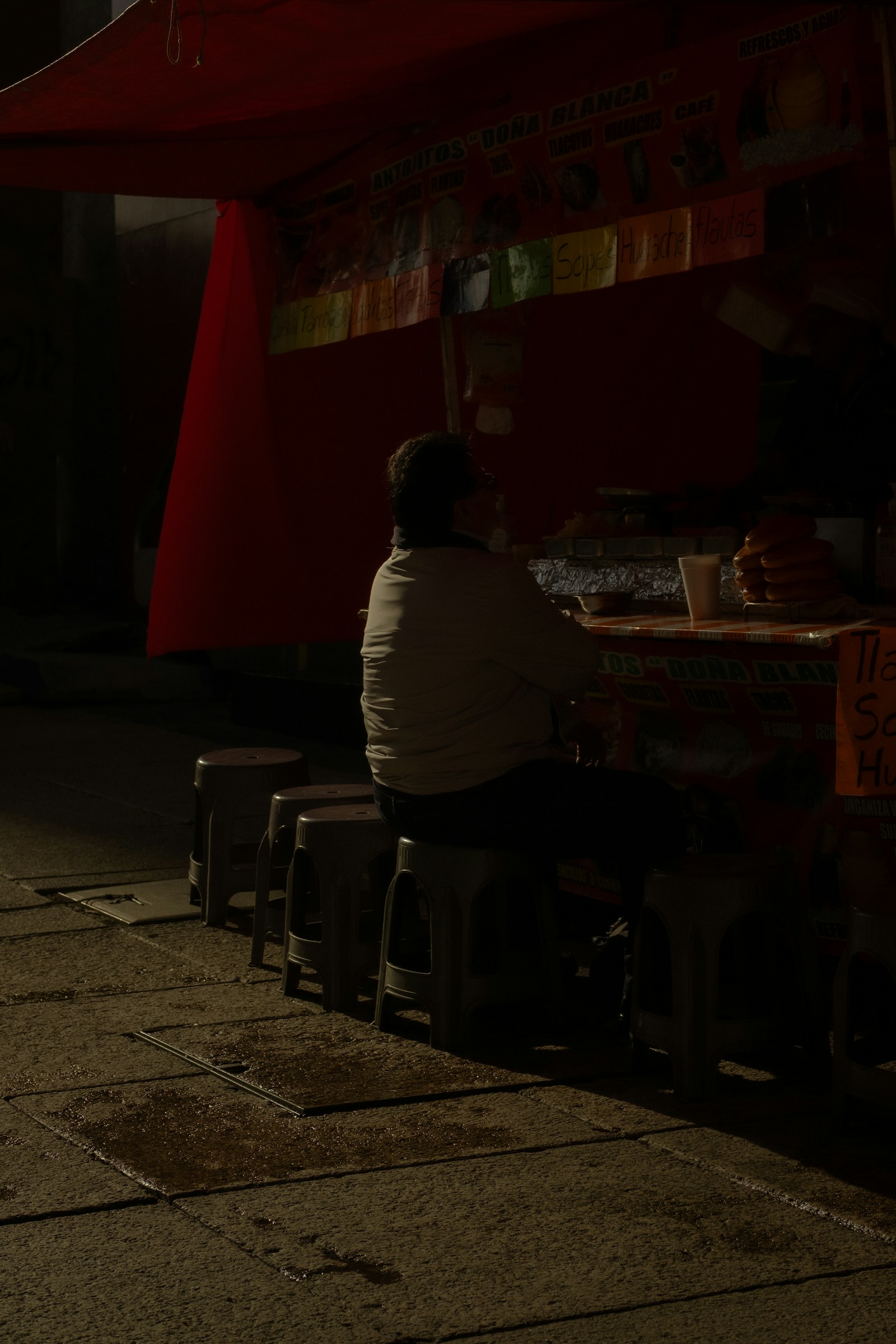 A person sitting alone at a dimly lit food stall late at night.
