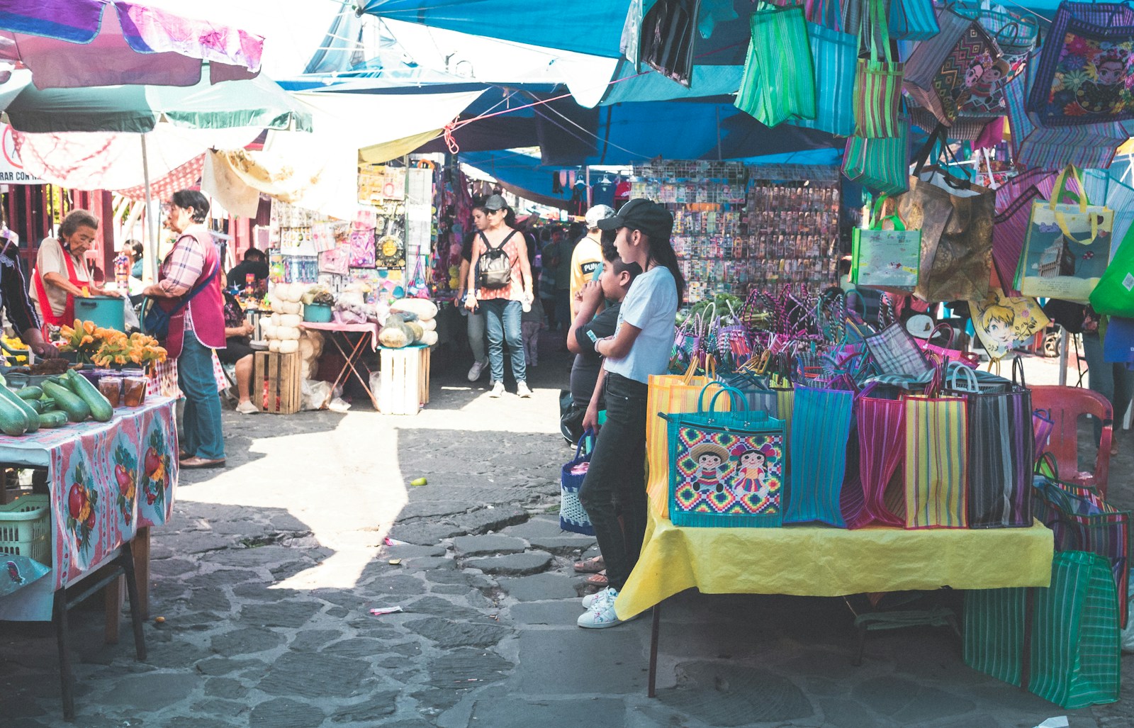 People walking among covered stalls at an outdoor street market.