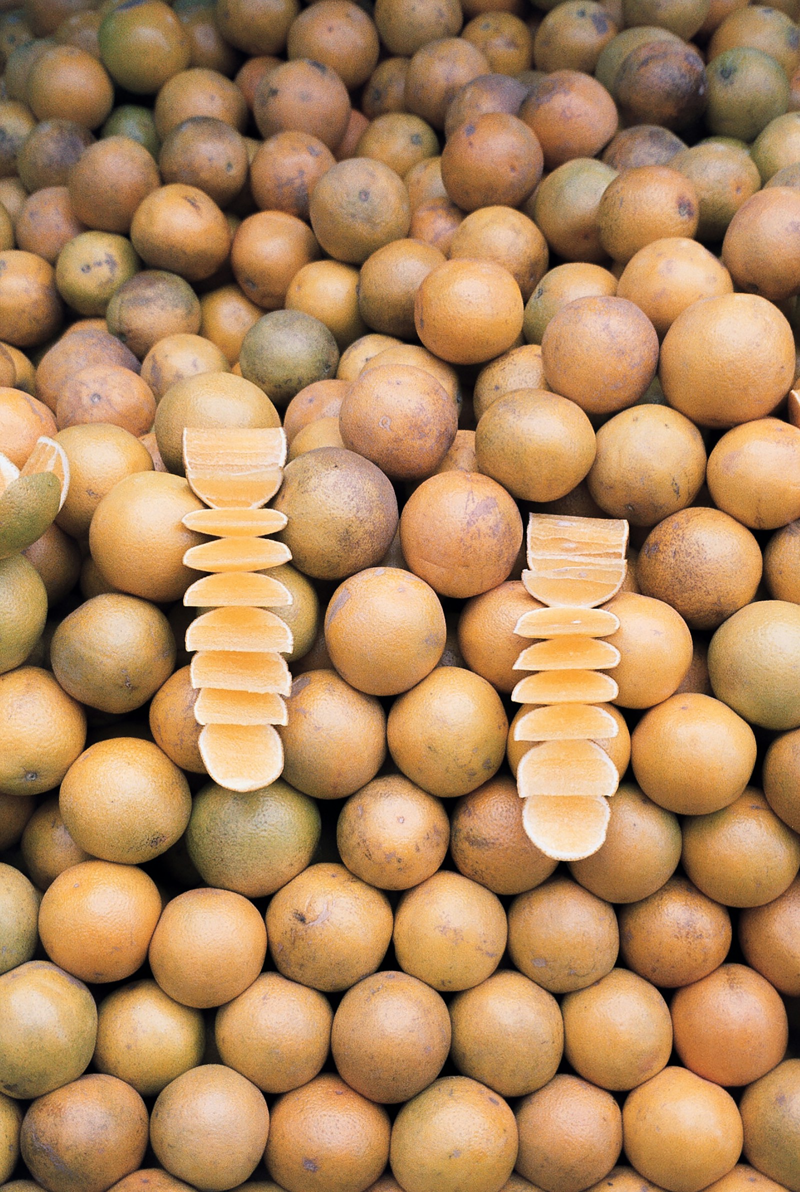A heap of round tan-skinned tropical fruit, two of them cut open on top.